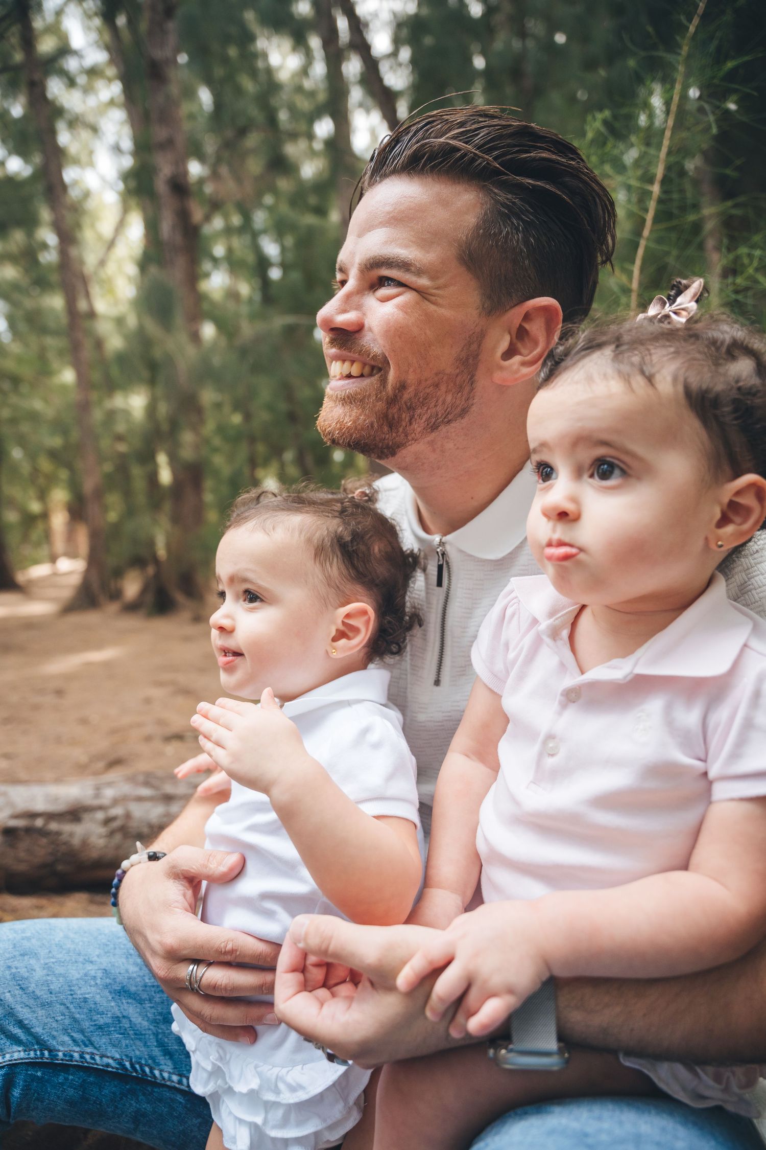 Parent and two small children sharing a tender moment outdoors in a forest setting.