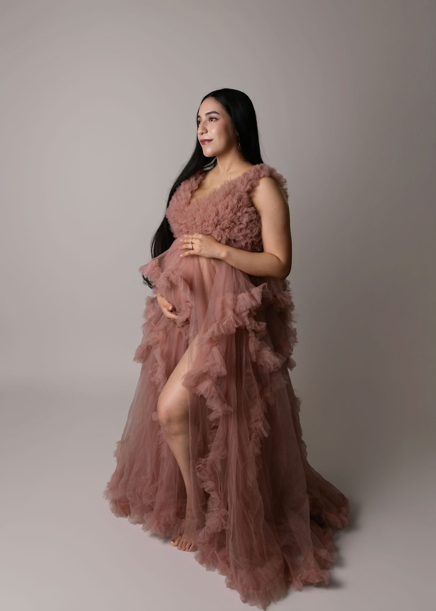 Elegant maternity photo featuring a flowing dusty rose tulle gown with ruffled layers against a neutral backdrop.
