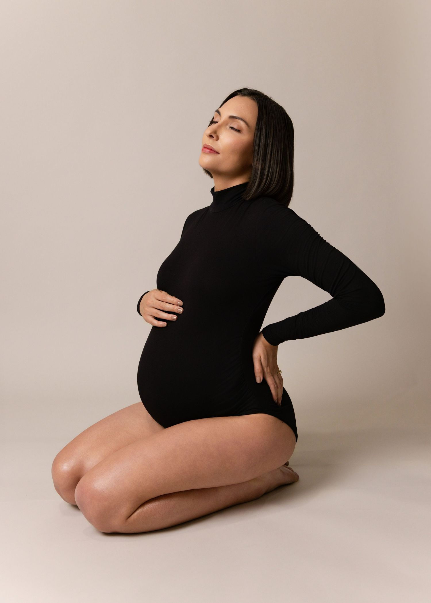 Elegant maternity photo featuring a black bodysuit pose against a neutral backdrop.