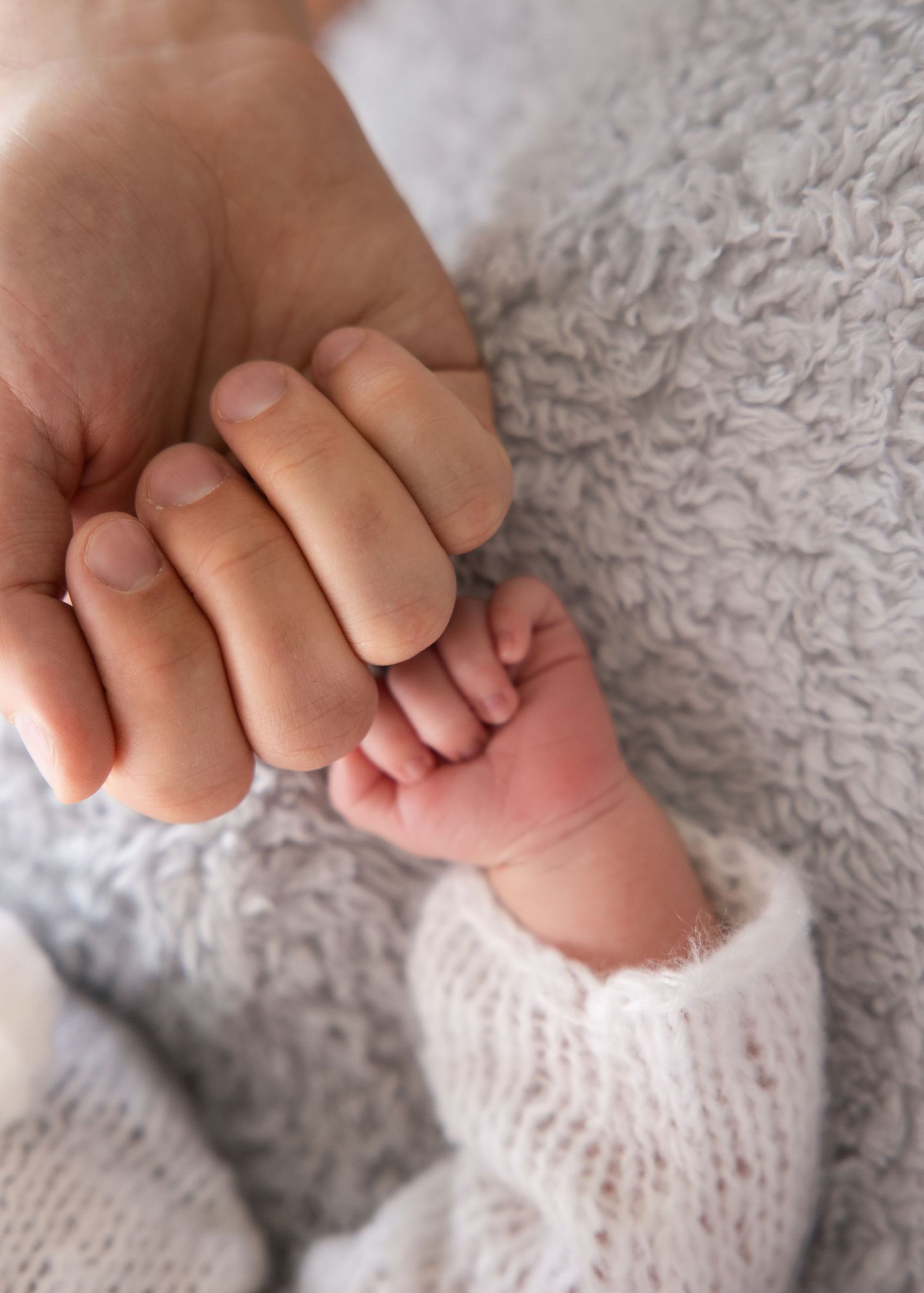 Utah newborn photographer detail photo — dad’s hands holding swaddled baby for scale