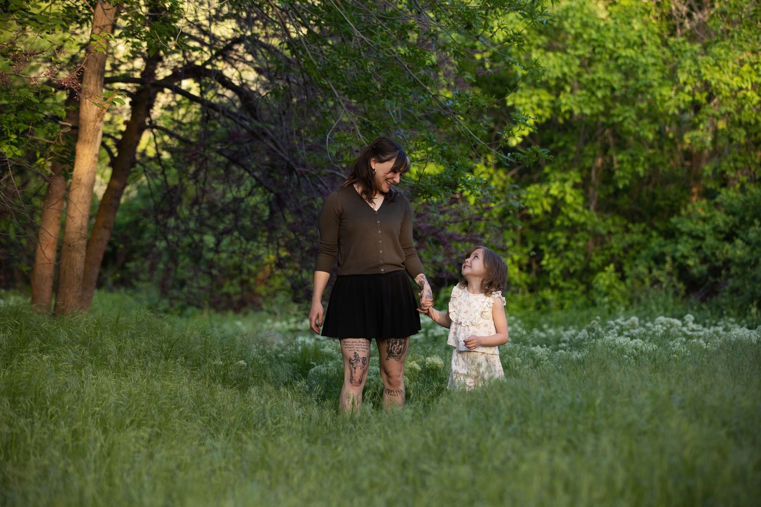 Two figures walk together through a lush green park setting during a warm summer evening.