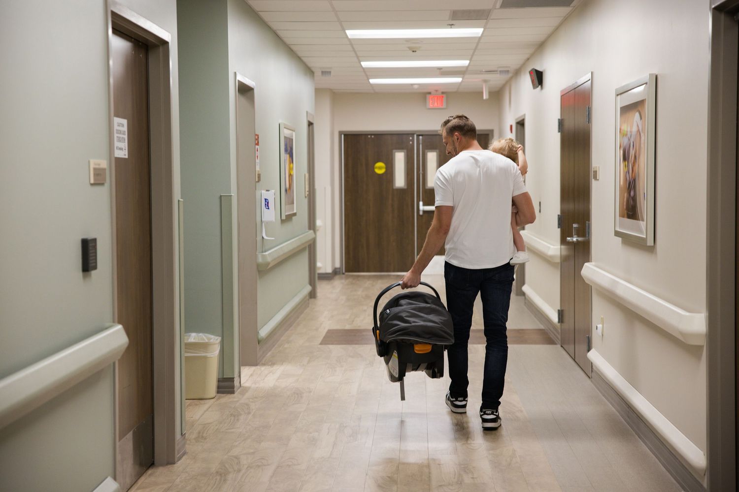 Medical professionals walk down a long hospital hallway with fluorescent lighting and white walls.