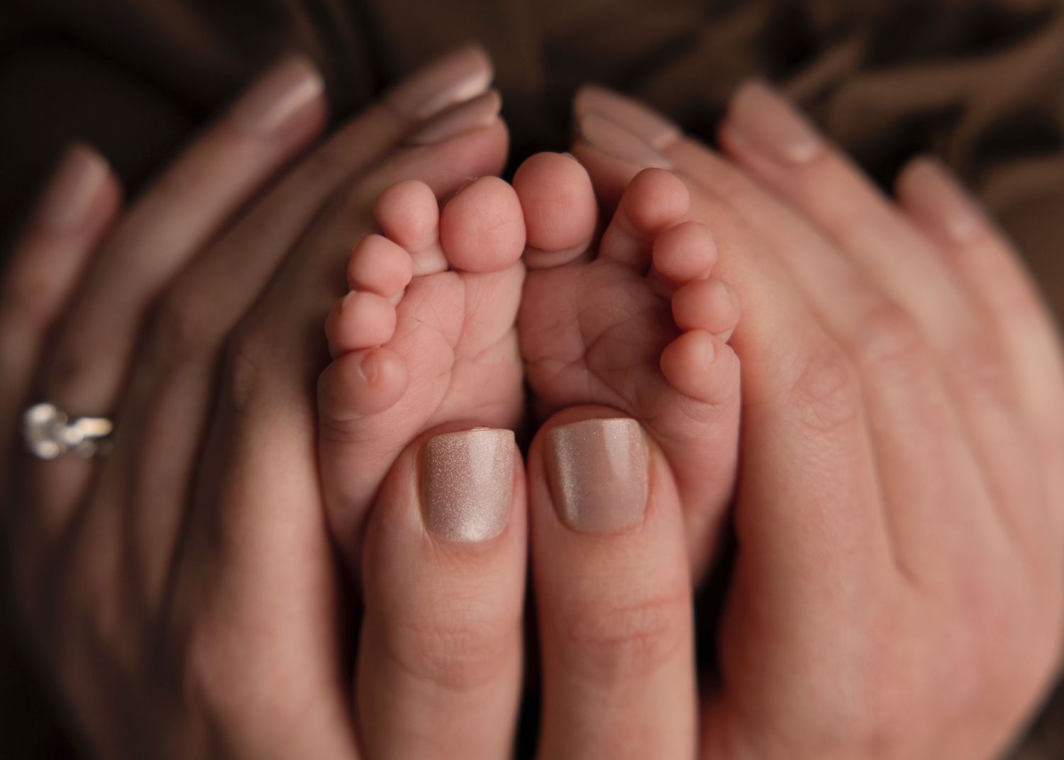 Adult hands gently cradling tiny baby feet against dark background in tender parenting moment.