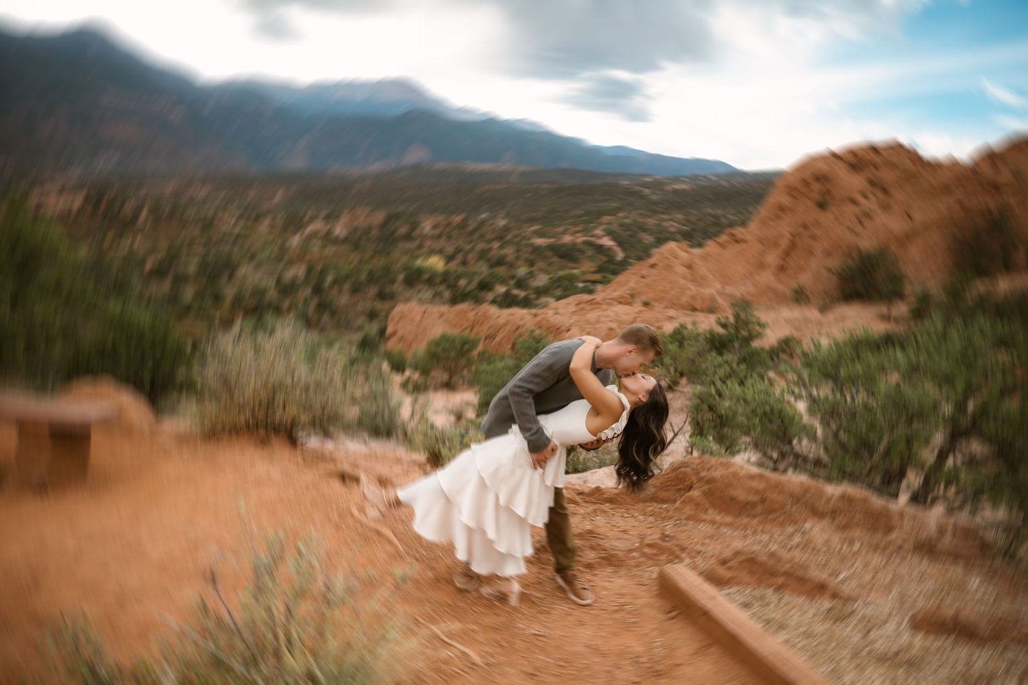 Dramatic dip pose during wedding photoshoot in desert mountain landscape.
