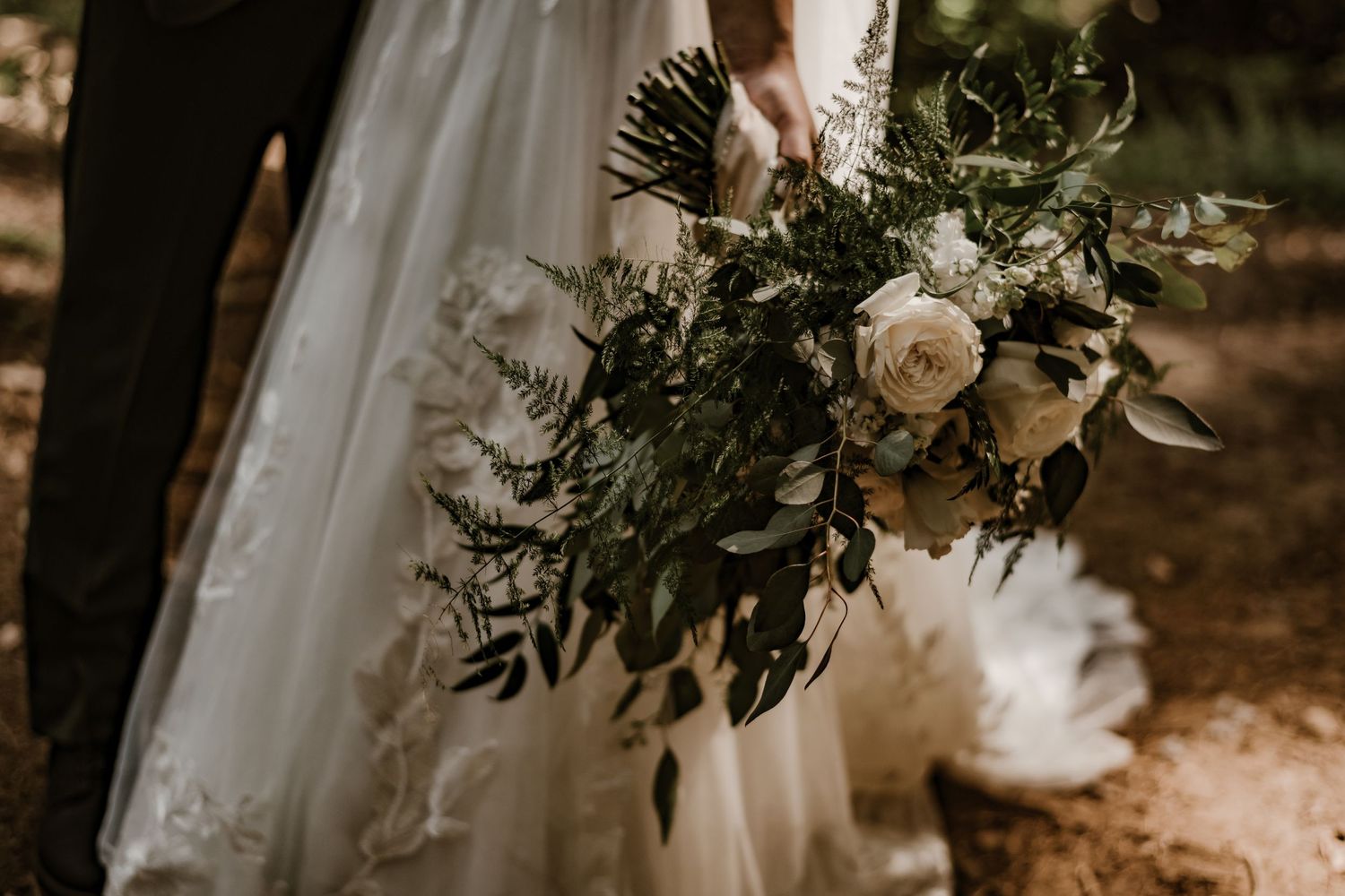 Elegant wedding bouquet with white roses and greenery against bridal dress.