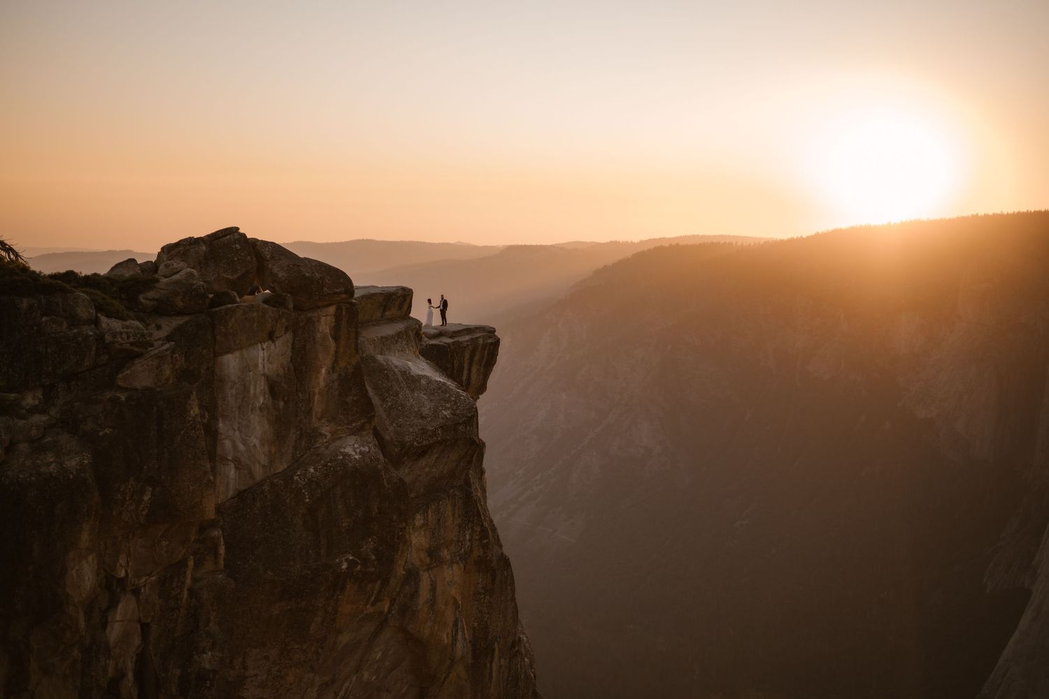 Photographer took elopement photos Silhouetted figures stand on cliff edge against dramatic mountain sunset landscape on the East Coast