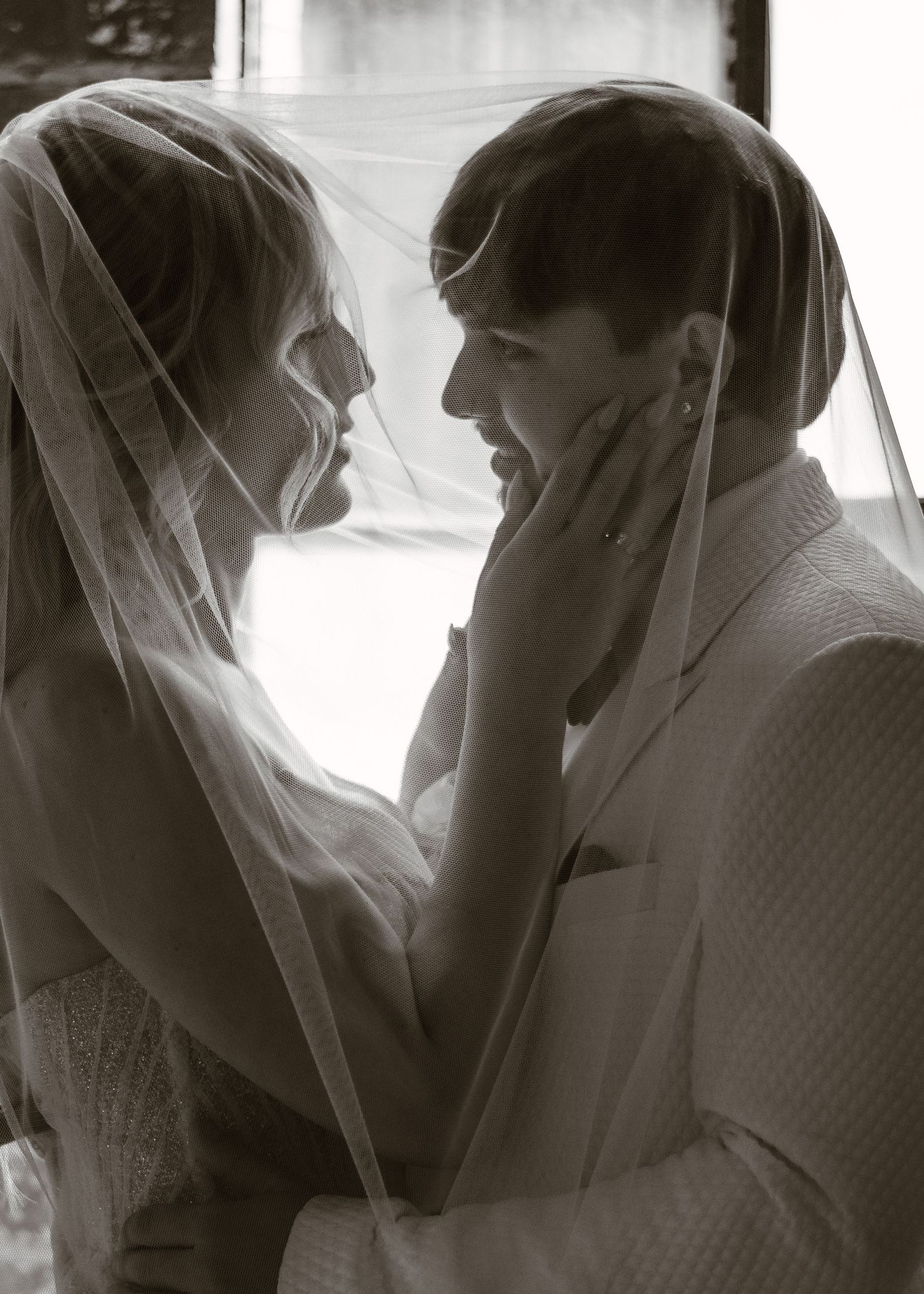 An intimate black and white photo of a couple under a wedding veil.