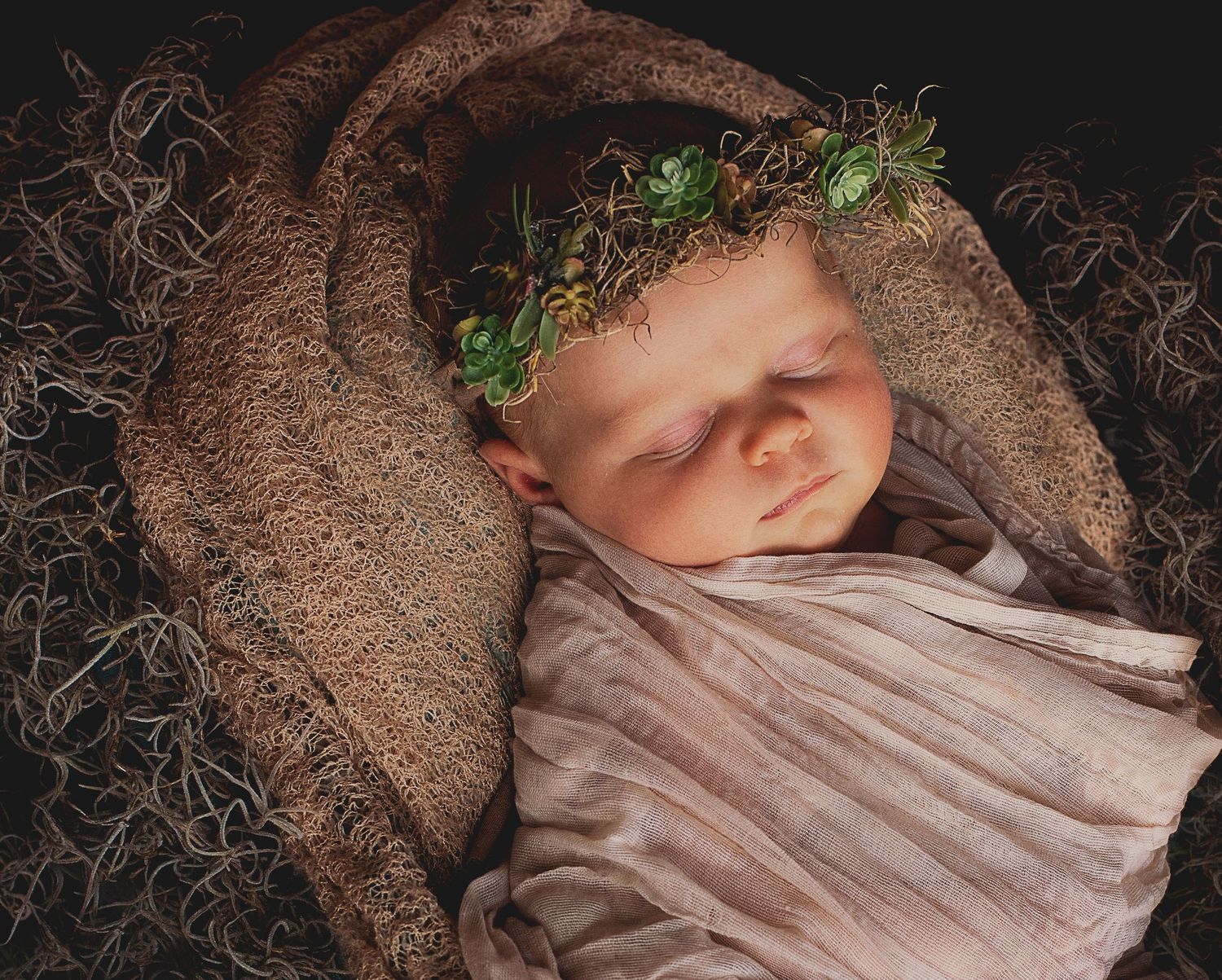 Artistic newborn photography series with baby wrapped in soft fabric against dark background.