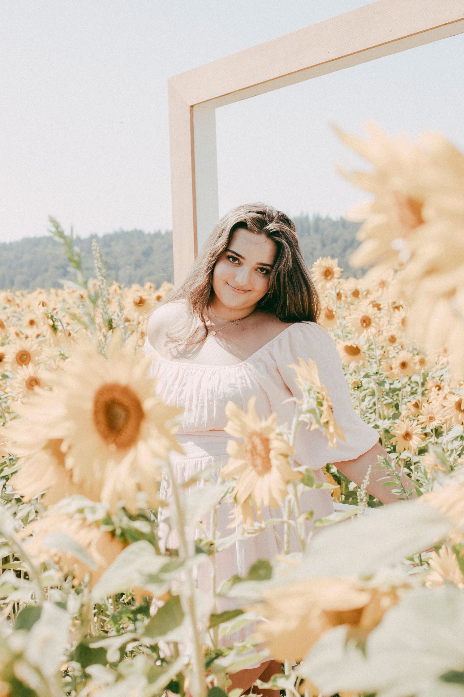 Ethereal portrait in a sunflower field with soft natural lighting and white summer dress.