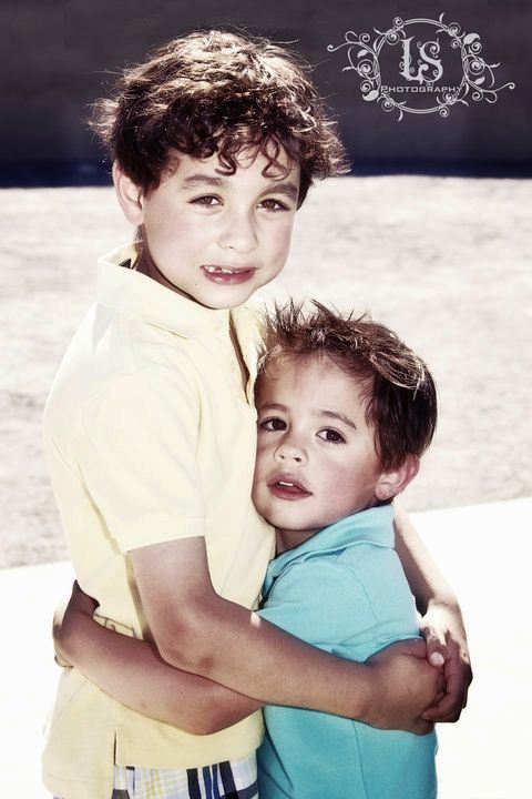 Siblings in yellow and blue shirts hugging and smiling in outdoor portrait series.