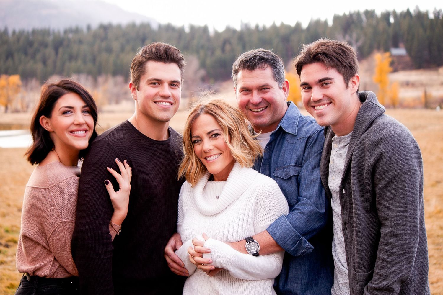 A cheerful group portrait captured in a scenic fall landscape with mountains behind them.