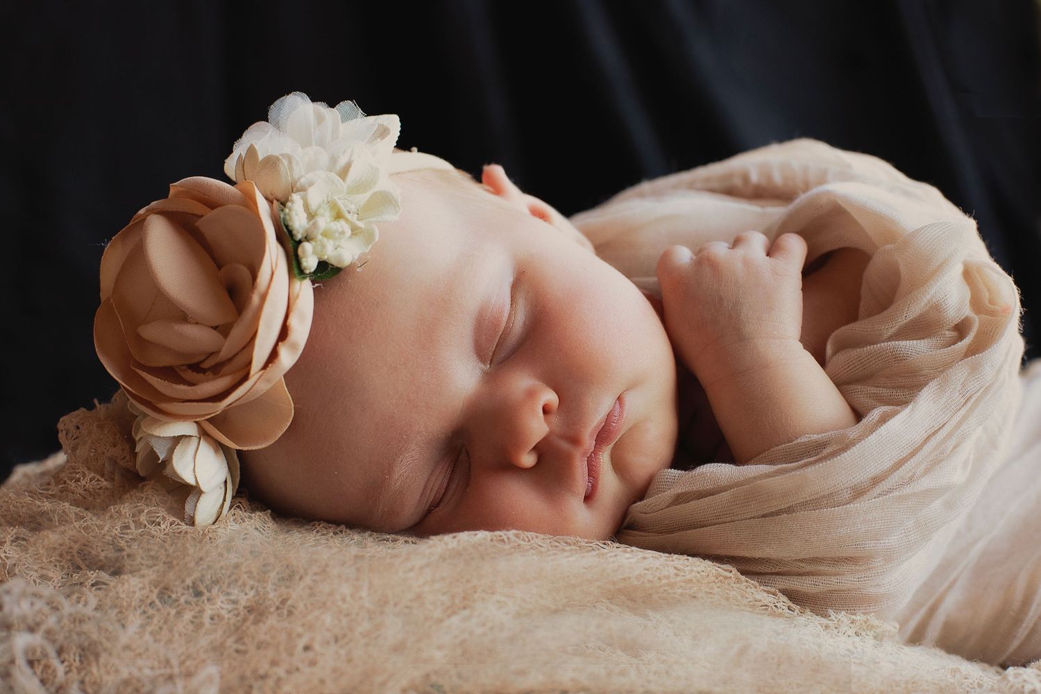 Close-up newborn photography with soft beige wrapping and natural lighting.