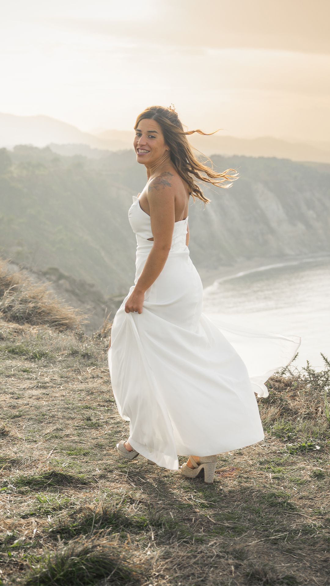 Espectacular ocaso en el reportaje de novios de post boda. Novia mira a su novio mientras corre por el Cabo Vidio en Asturias.