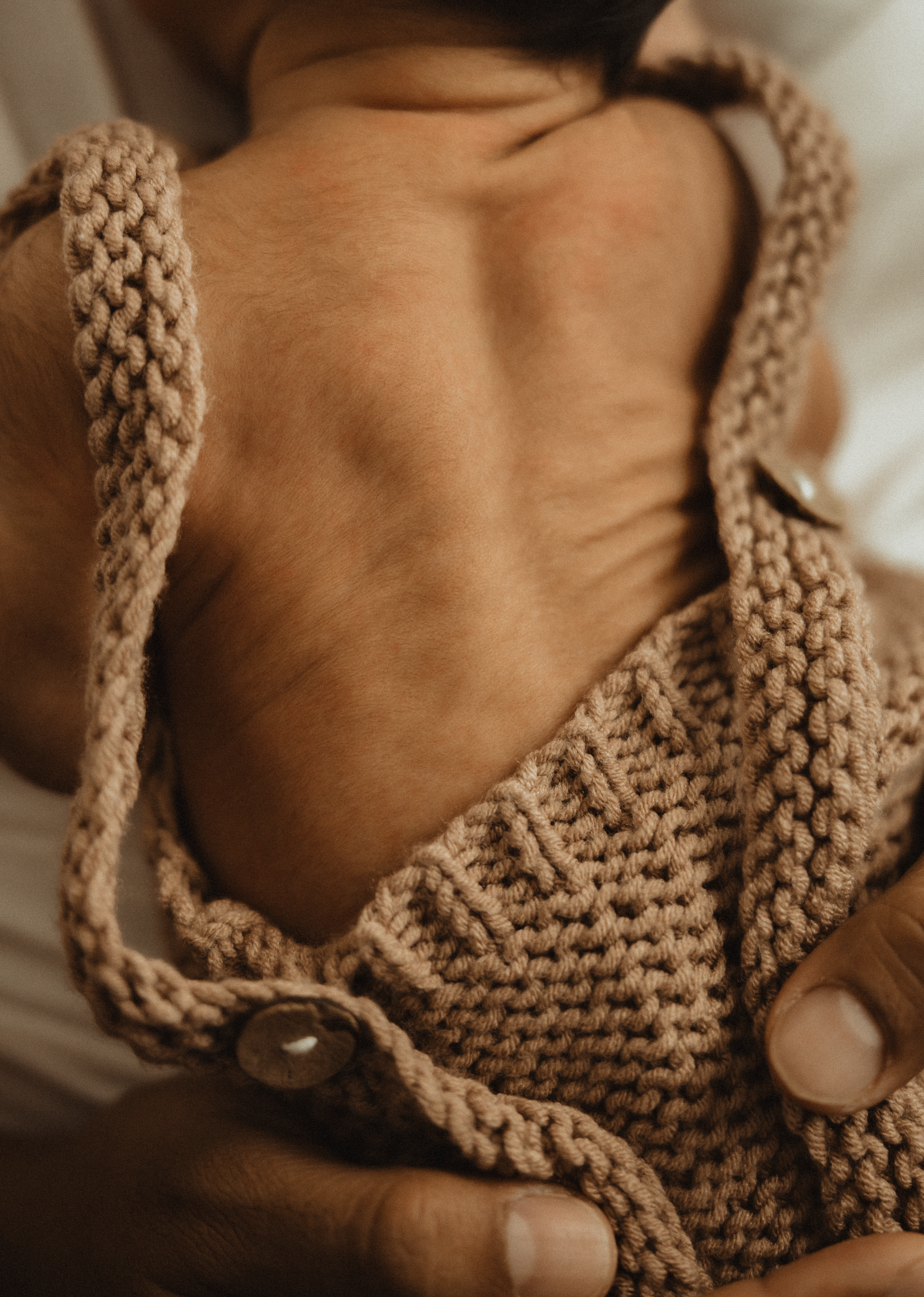 Close-up of a baby wearing a chunky knit tan romper with button details, showing their bare back.
