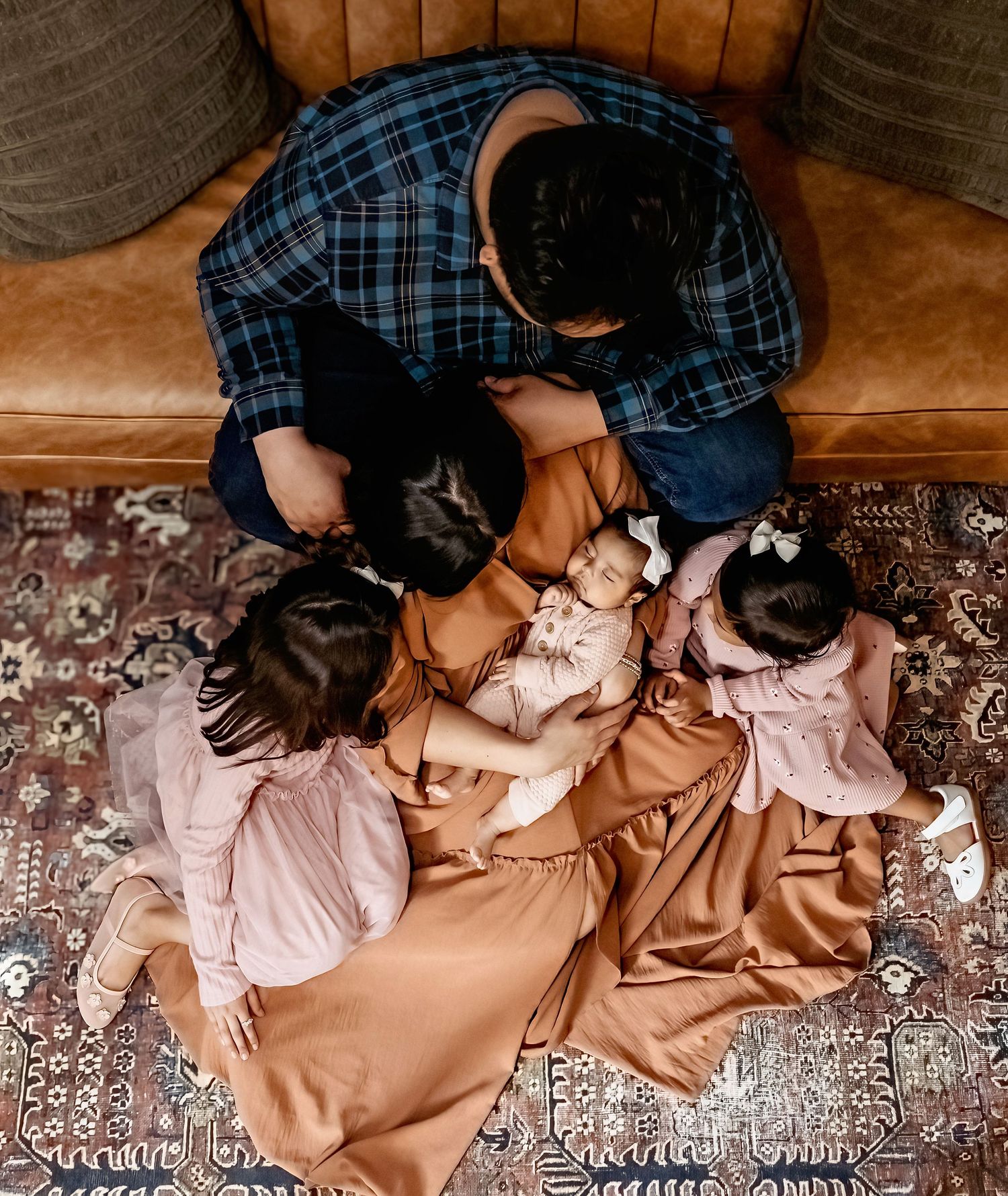 Overhead view of family cuddles on patterned rug in cozy home setting.