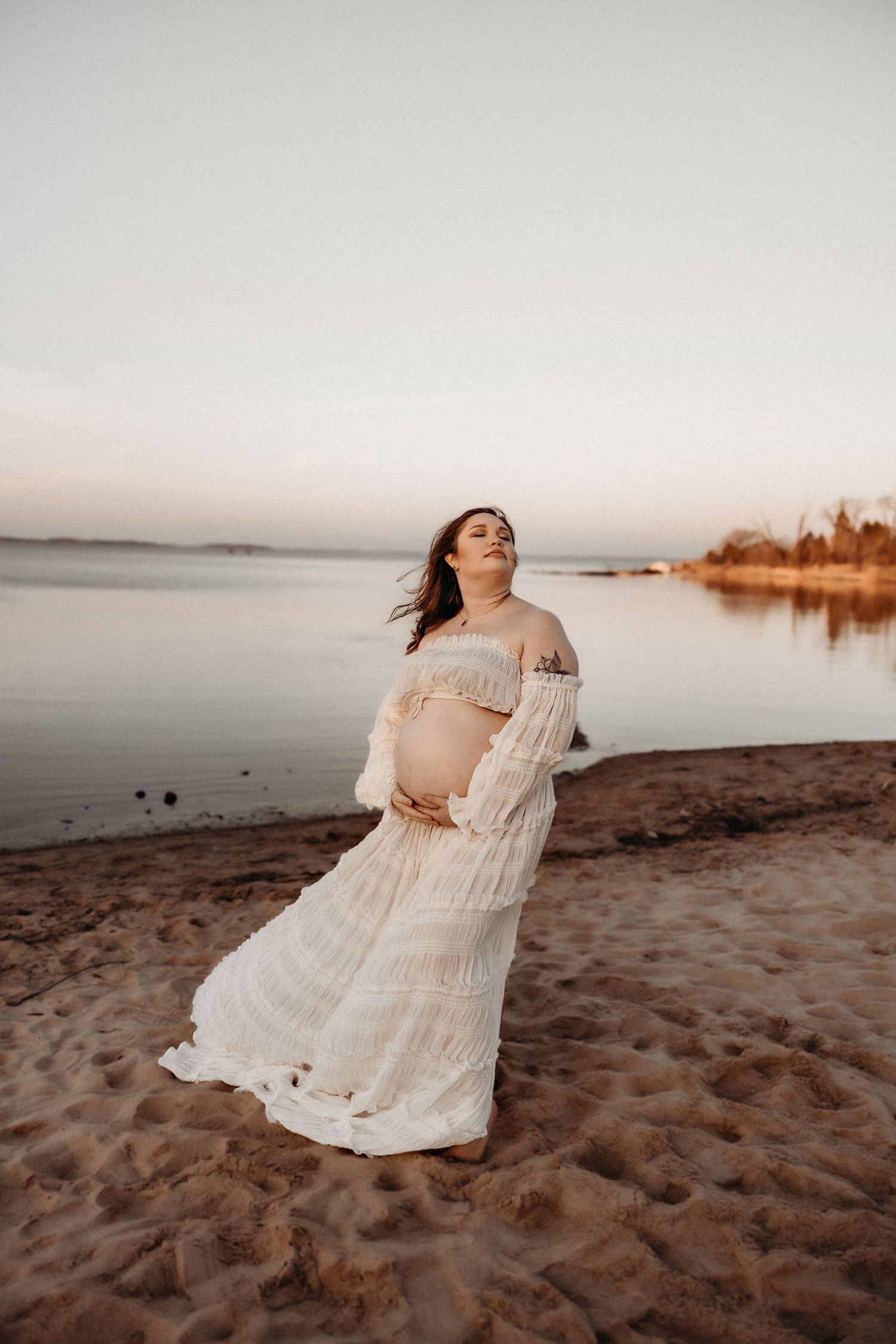 A romantic sunset beach photoshoot featuring a flowing white lace dress against a serene coastal backdrop.