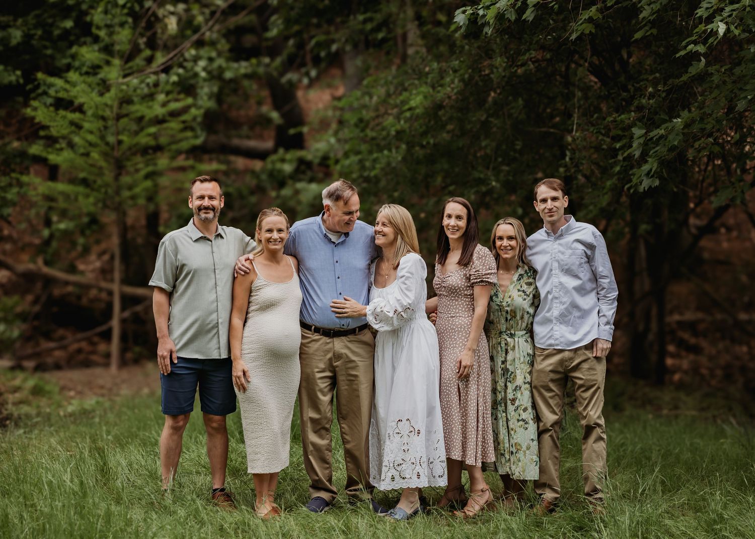 A group of people walking together and laughing in a lush green outdoor setting during summer.