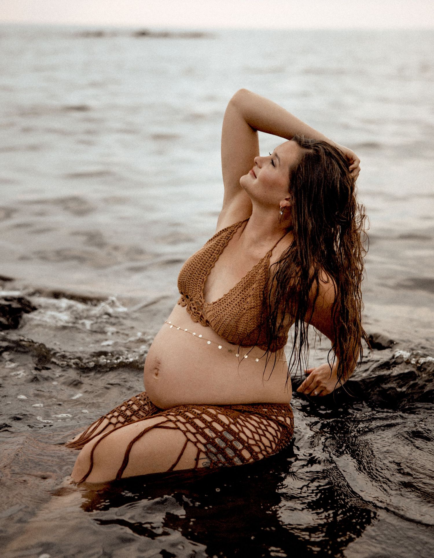 A person in a netted swimsuit poses dramatically in shallow ocean water during sunset. Kent Island Maryland Maternity Session