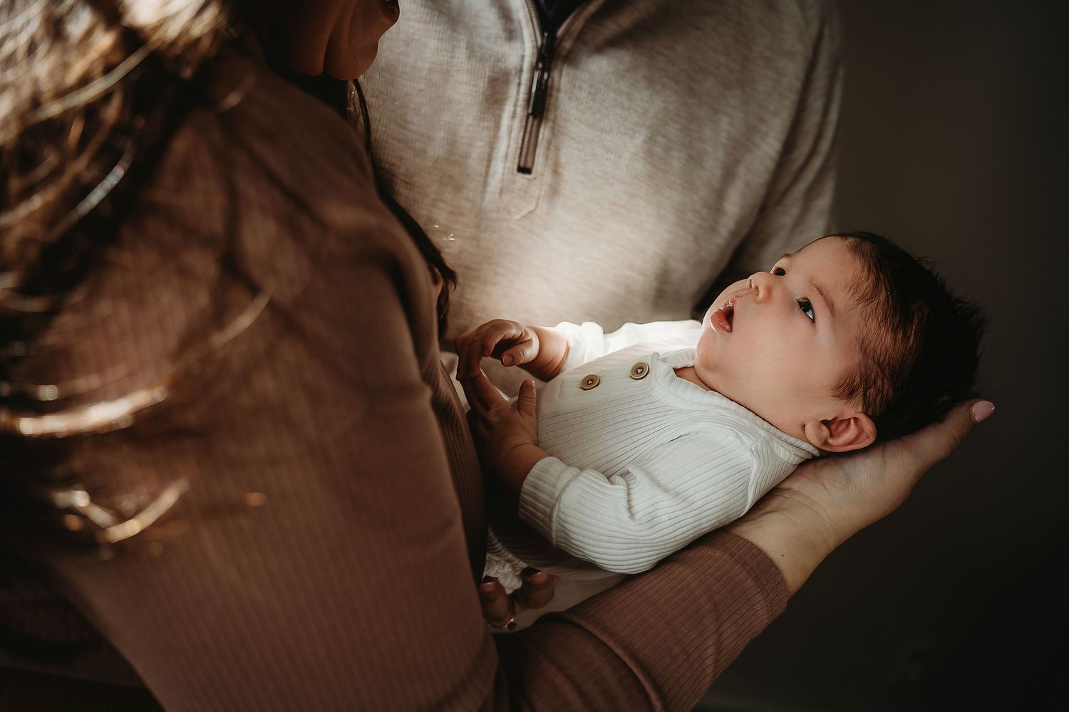 A baby in a white onesie lies on a brown surface while being fed from a bottle.