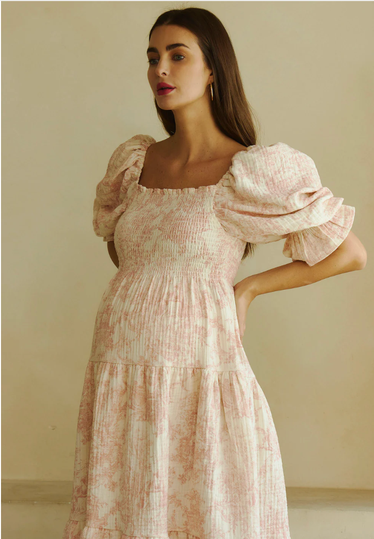 Woman wearing a pink floral smocked bodice midi dress with puff sleeves and tiered skirt.