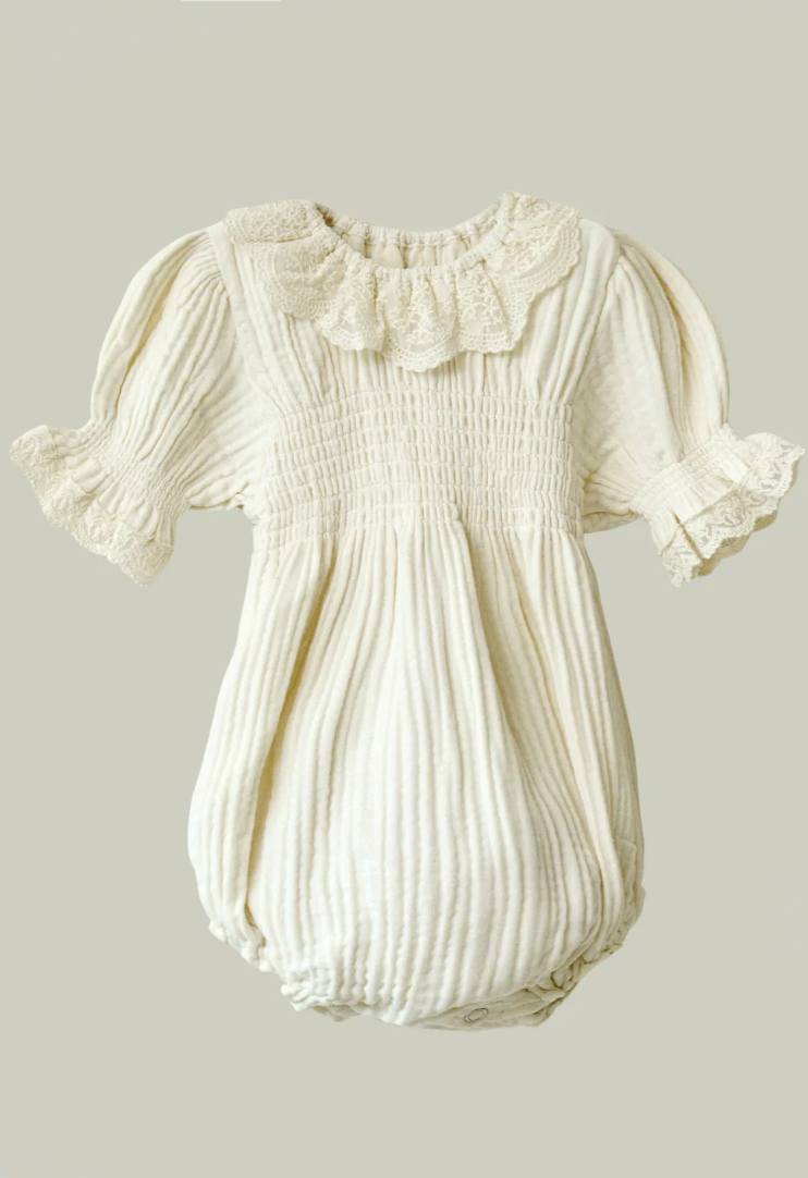 Ivory cream baby romper with lace collar, puff sleeves, smocked bodice, and bubble bottom in soft cotton fabric.