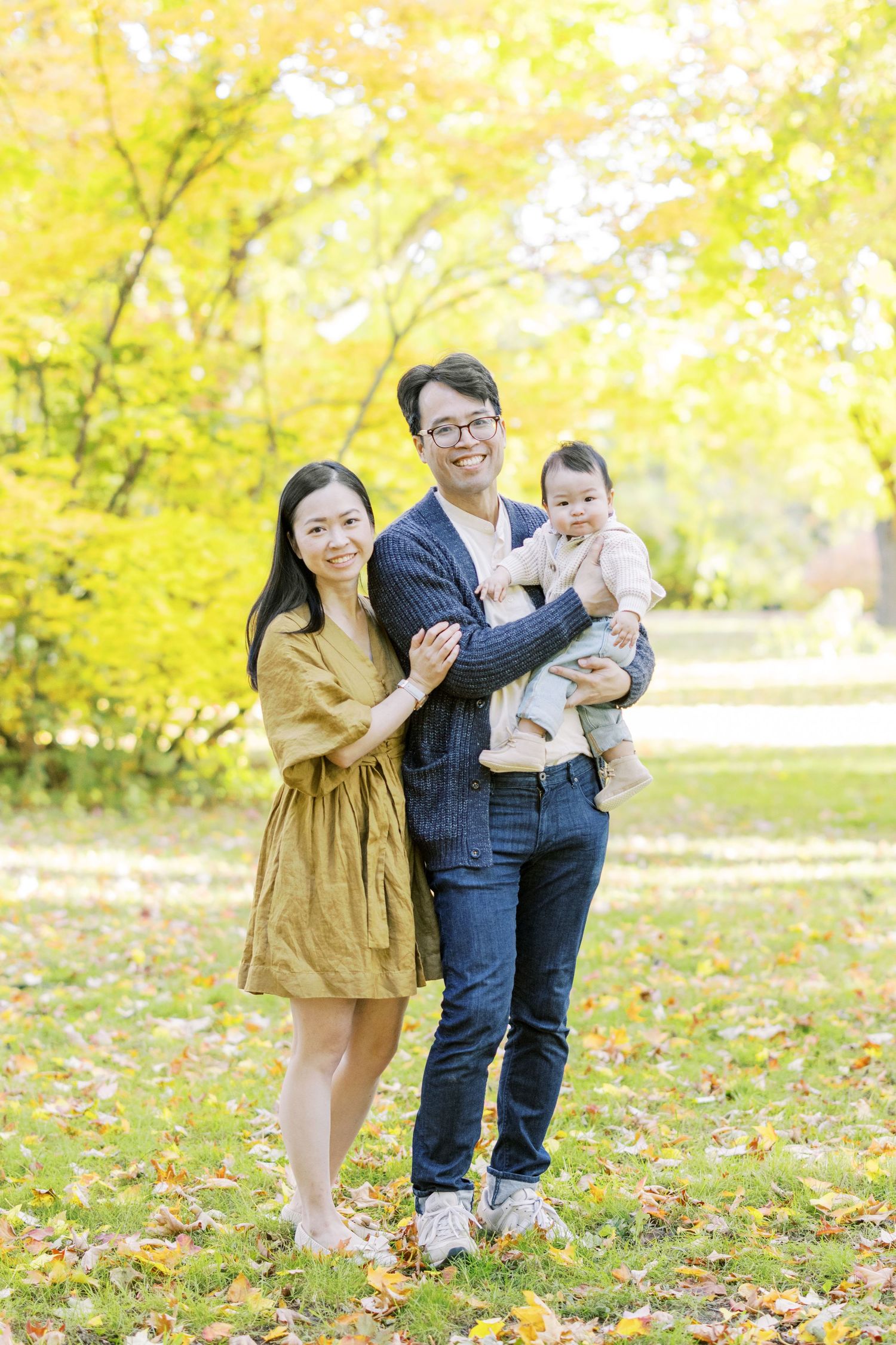 Happy Asian family of three posing together in autumn park with yellow foliage.