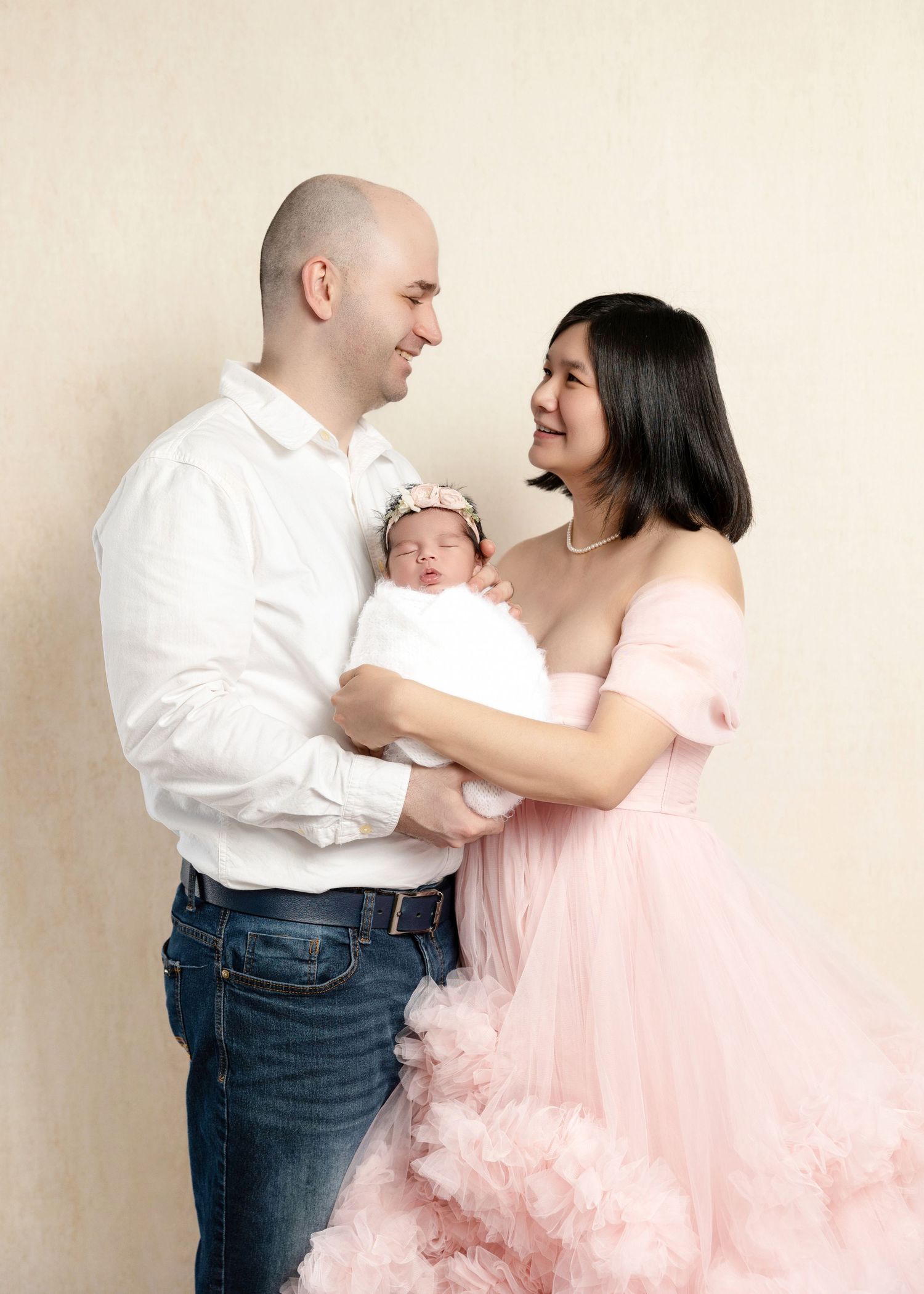 Happy parents in coordinating outfits lovingly holding their newborn baby girl in pink wrap.