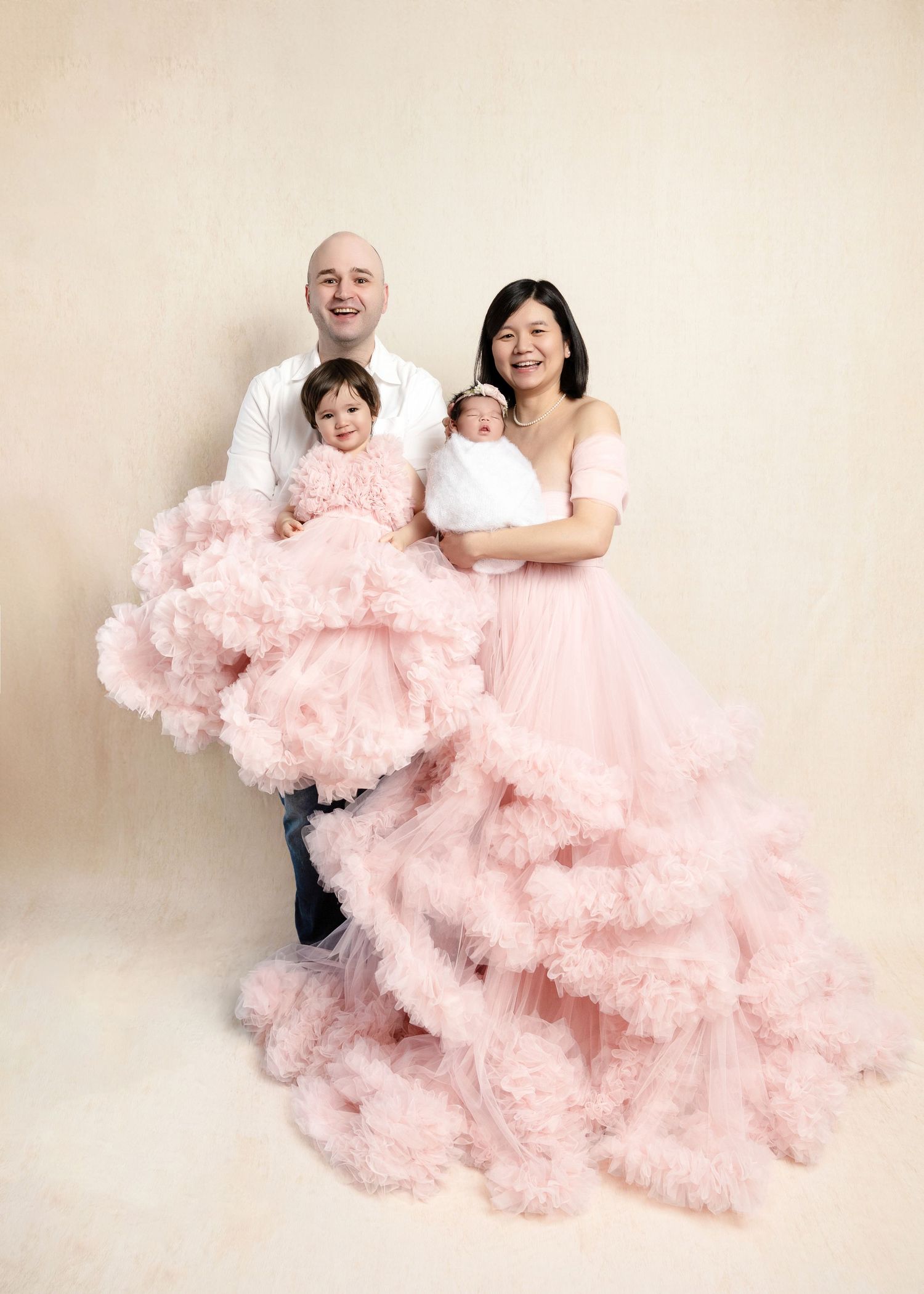 Family of four posing together with newborn baby and toddler in matching pink tulle gowns.