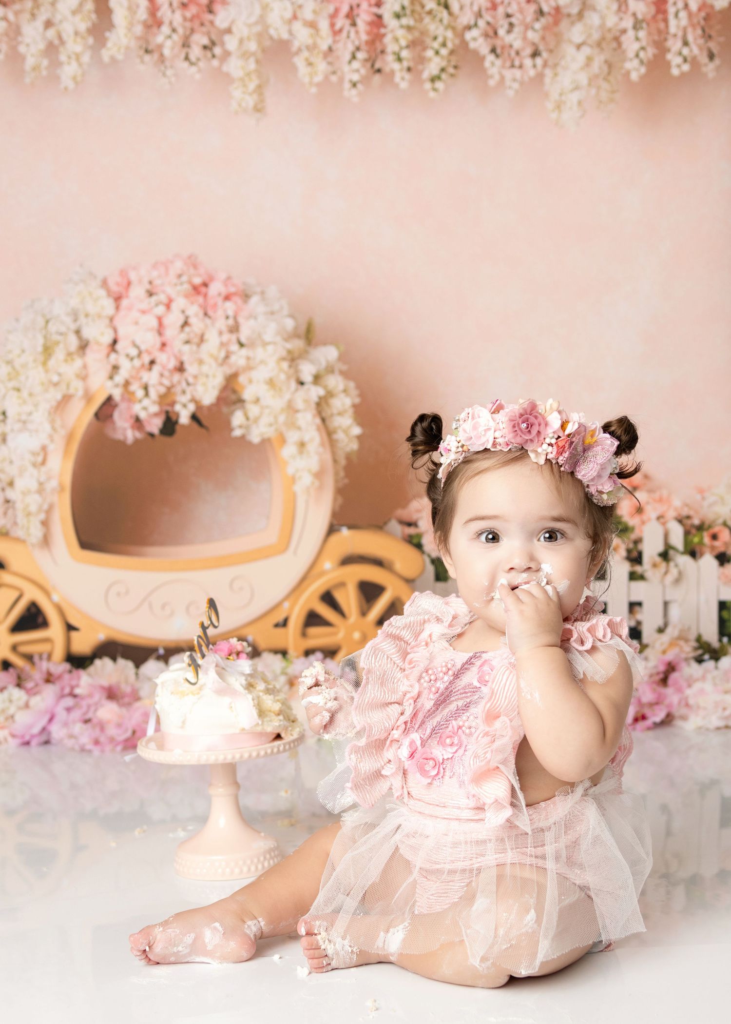Baby girl in pink lace dress eating birthday cake during a princess cake smash session.