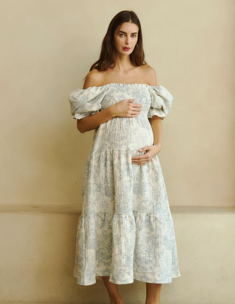 Pregnant woman wearing an off-shoulder white floral midi dress with puff sleeves and tiered skirt.