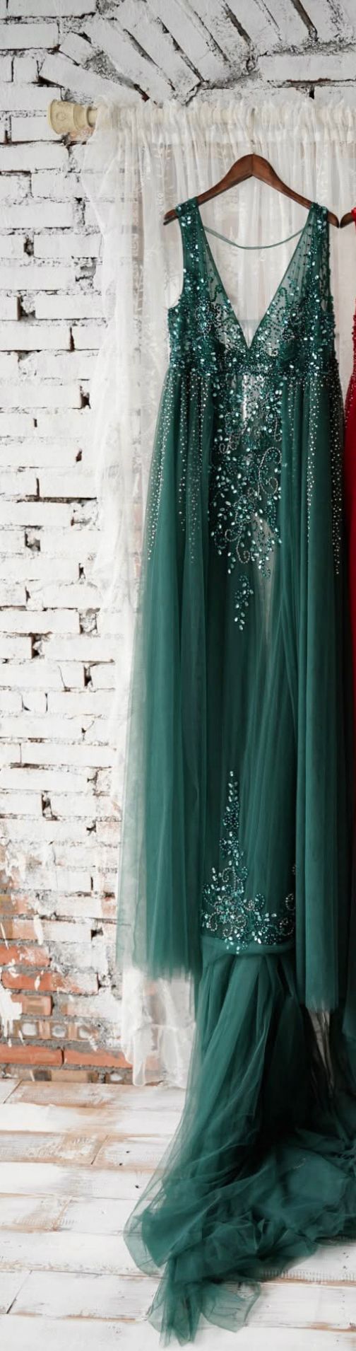 Elegant emerald green beaded tulle gown with V-neckline and crystal embellishments hanging on a wooden hanger.
