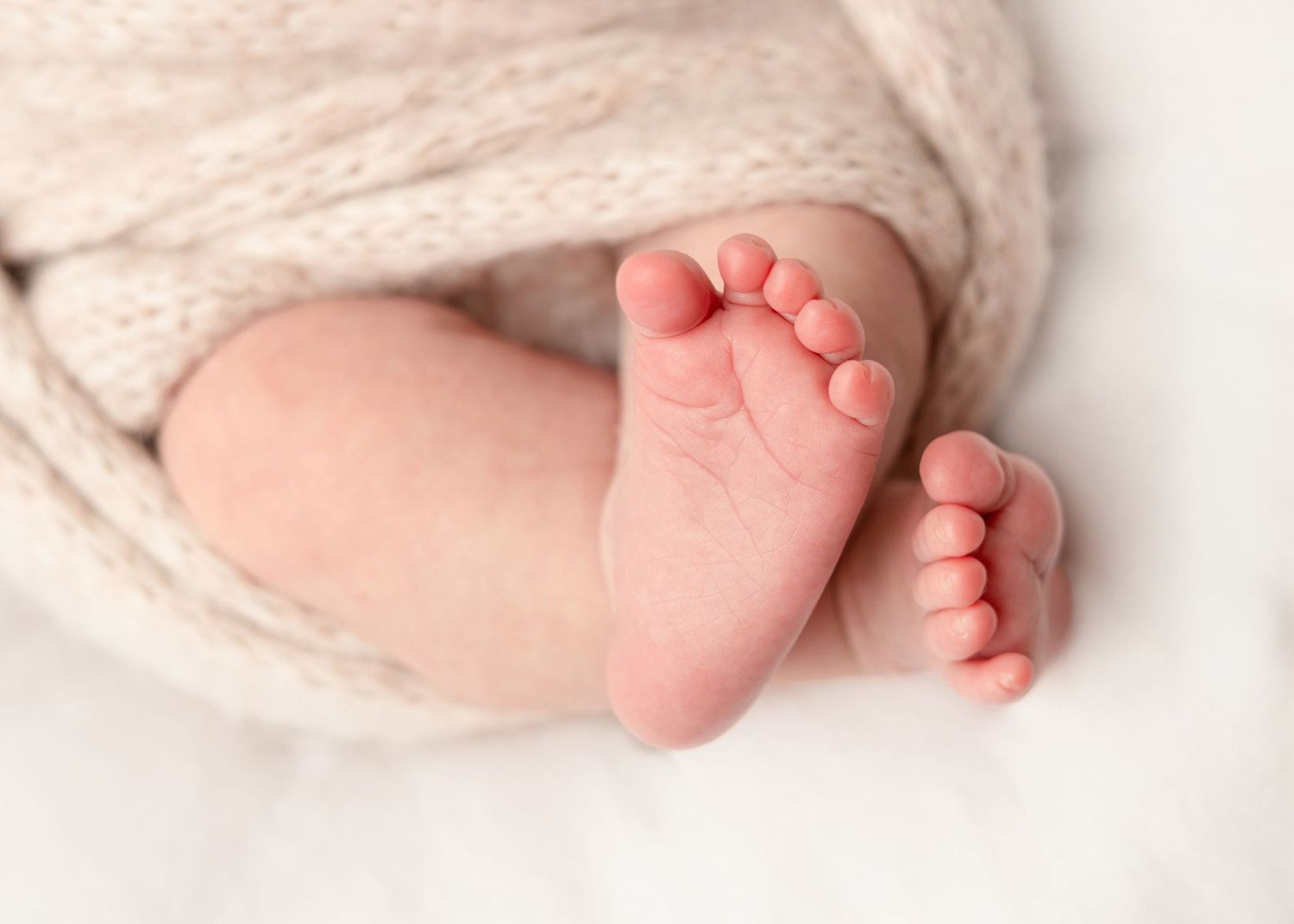 Close-up of tiny newborn baby feet wrapped in a soft cream knit blanket.