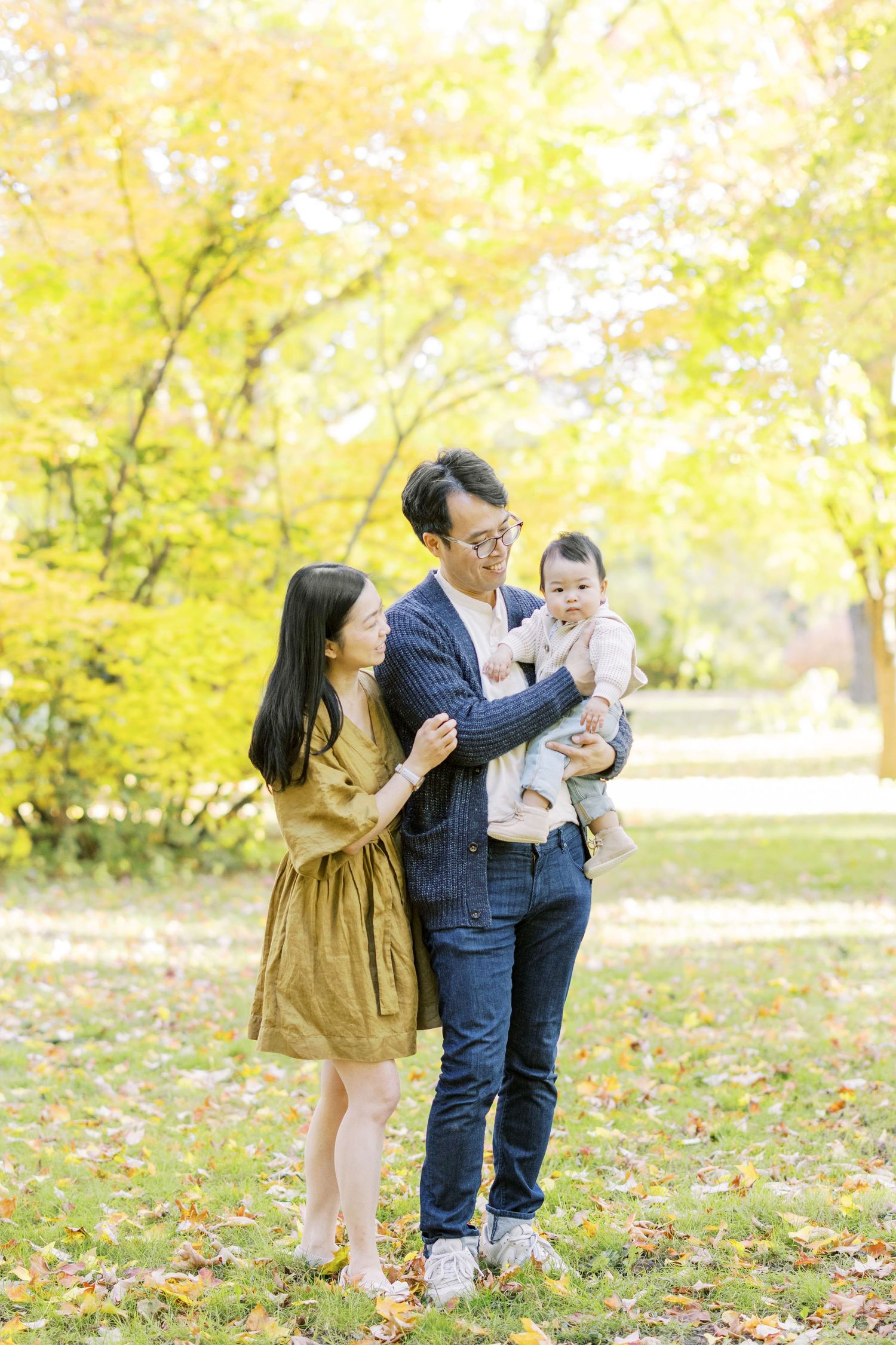 Asian family with mother, father, and baby enjoying autumn park with golden leaves.