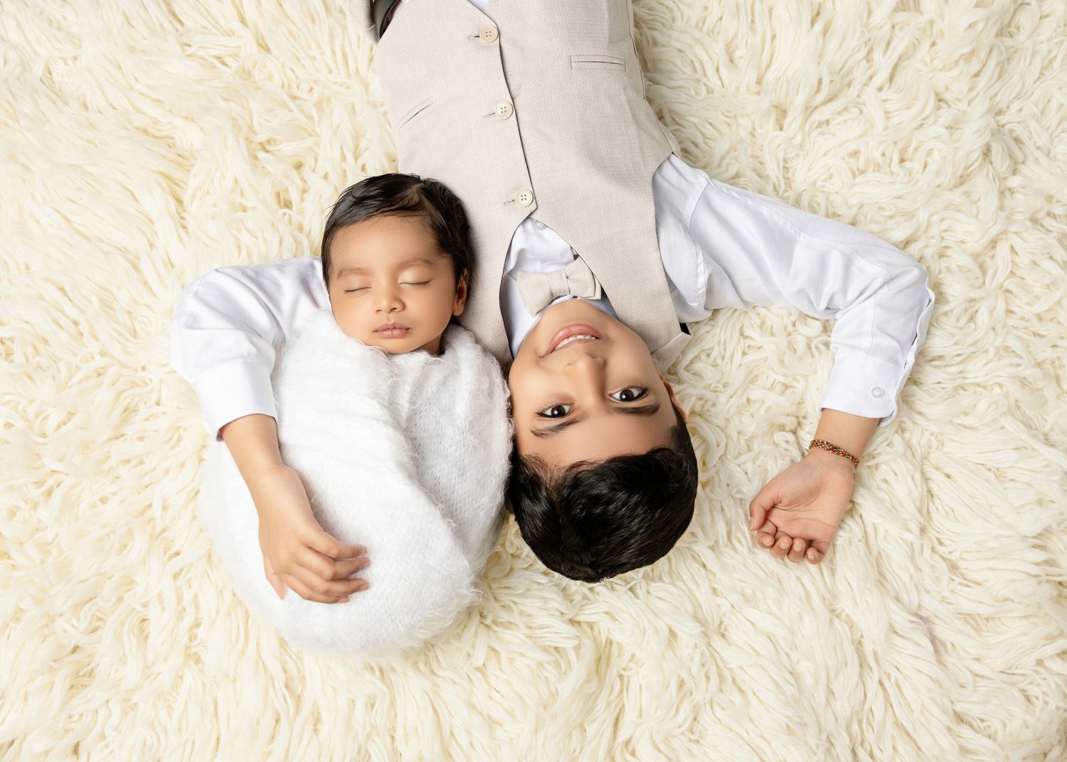 Father and newborn baby lying together on a fluffy white rug, both wearing white outfits.