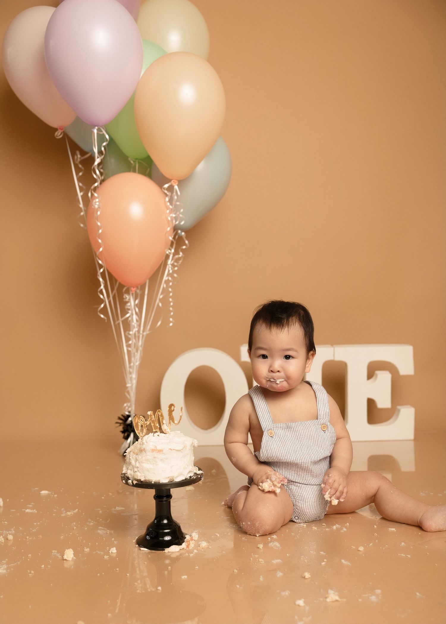 Baby's first birthday cake smash with pastel balloons and ONE letters on warm beige background.