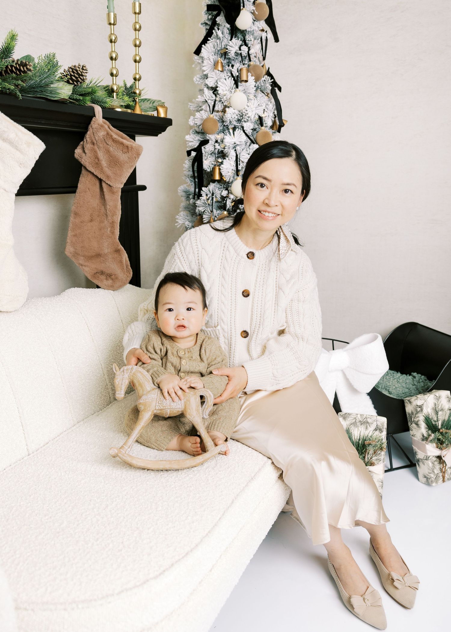 Mother and baby in matching cream outfits beside a white Christmas tree with gold accents.