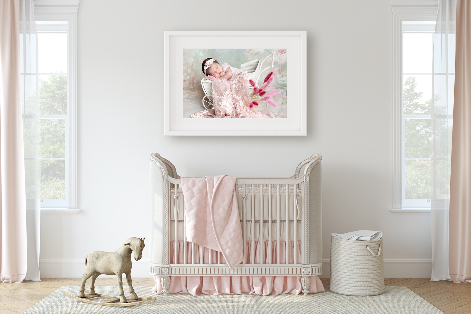 Framed newborn photo above a white crib in a soft pink nursery with rocking horse decor.