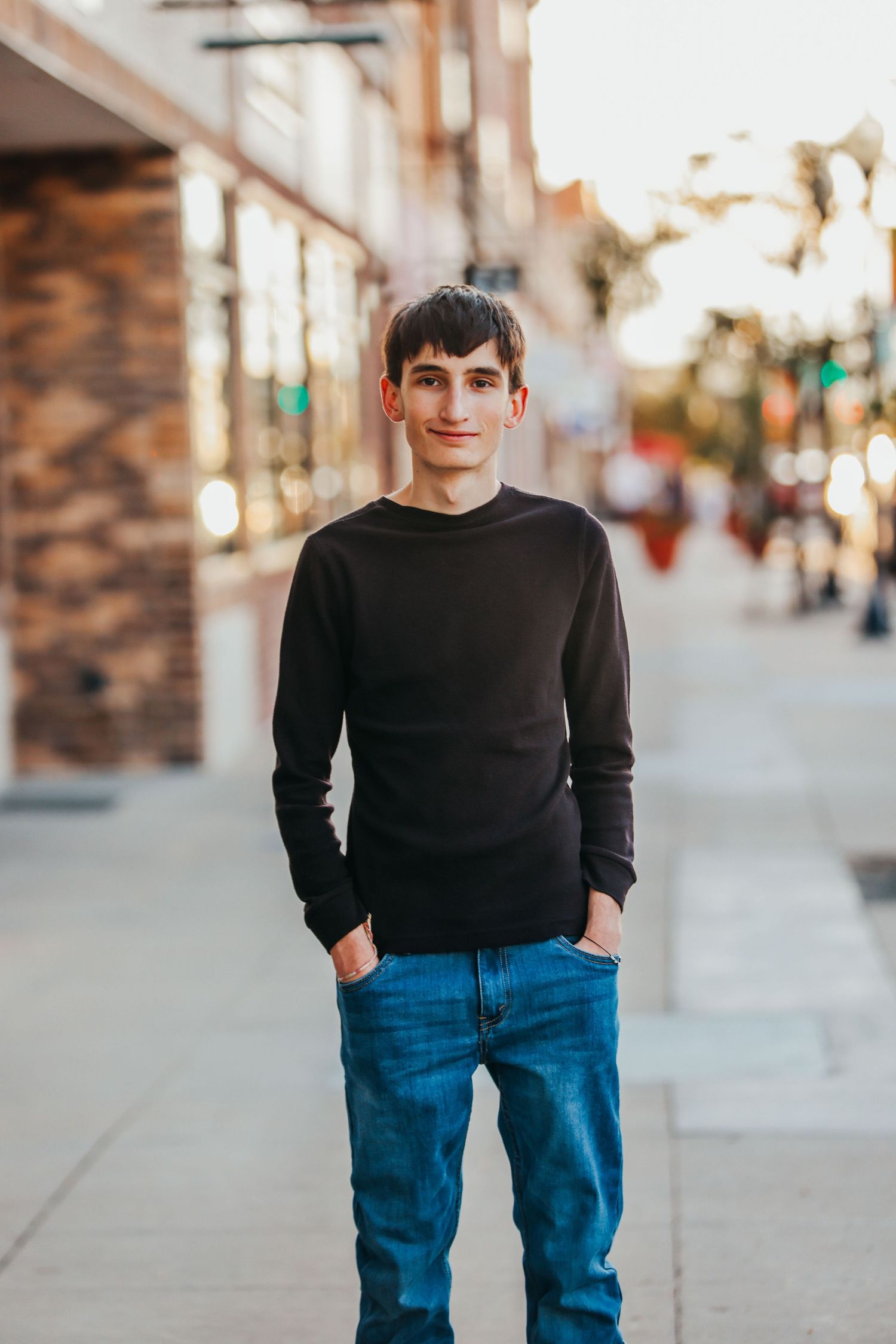 Casual street portrait of someone in a black sweater and jeans against an urban backdrop.