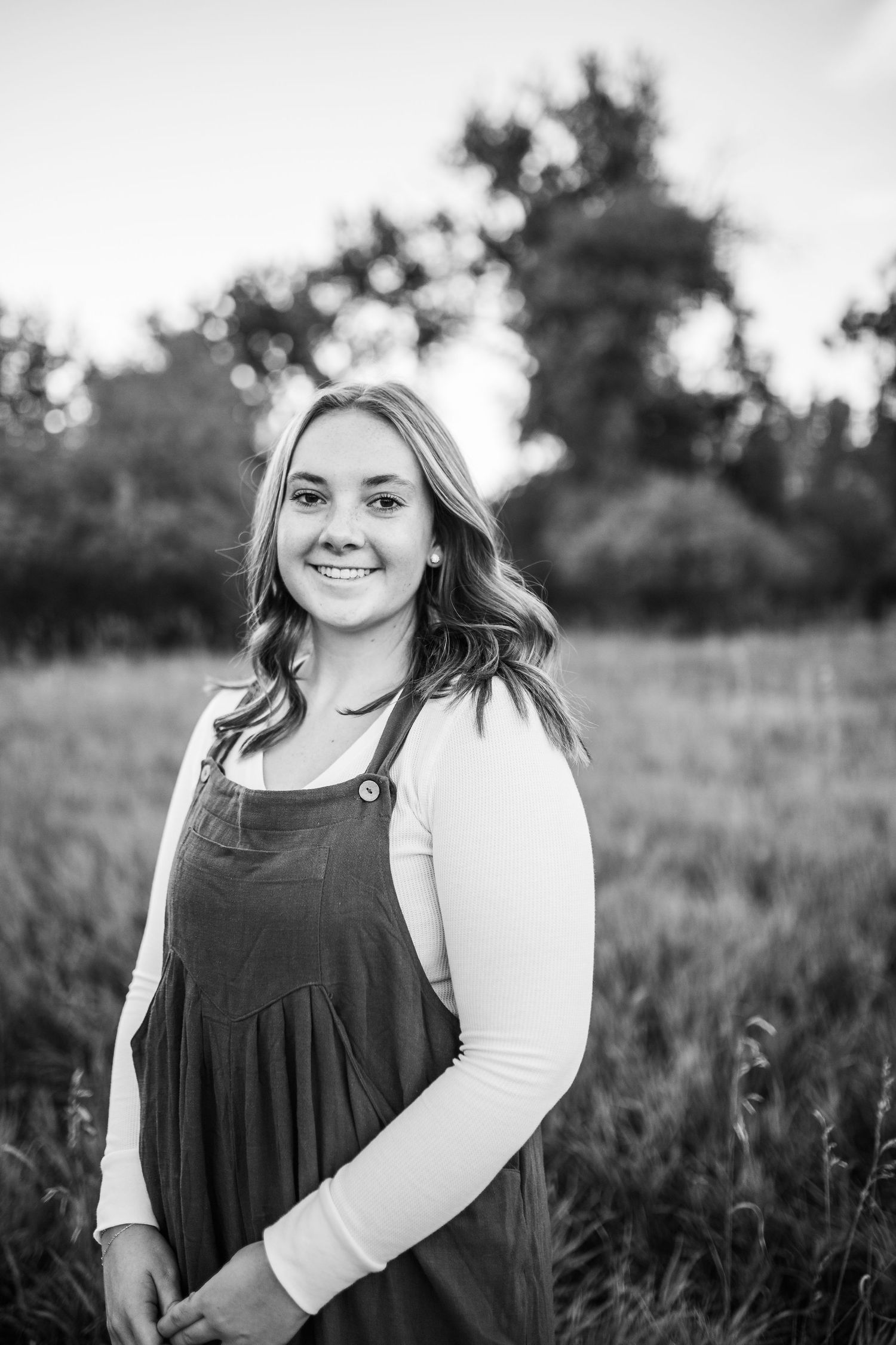 Black and white portrait of person in overalls standing in field.