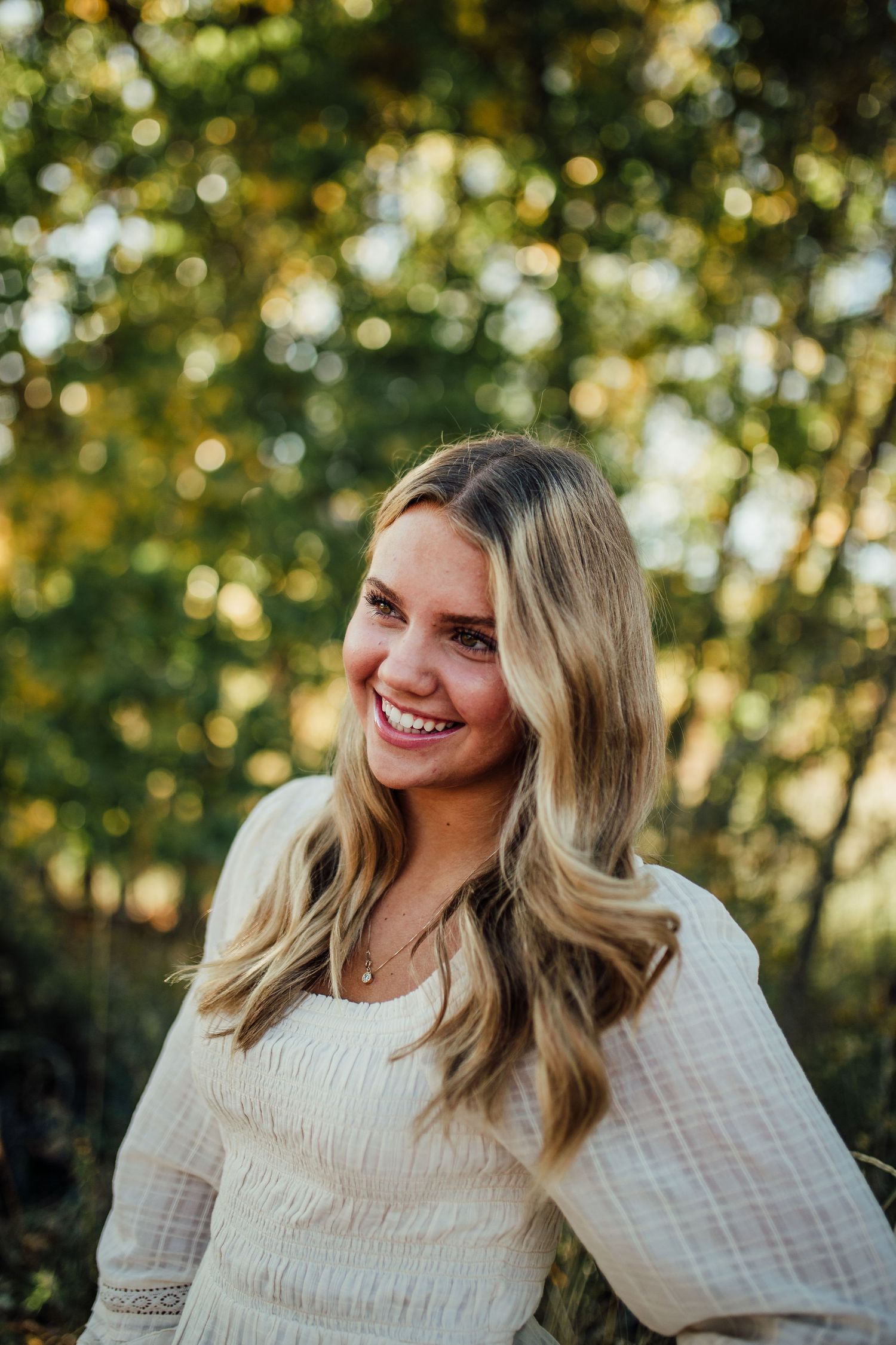 A casual outdoor portrait with bokeh trees in the background and warm natural lighting.