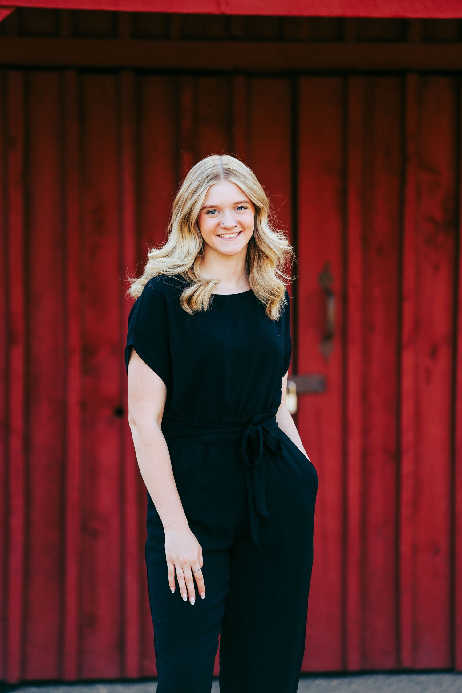Portrait against a striking red barn wall wearing an elegant black jumpsuit.
