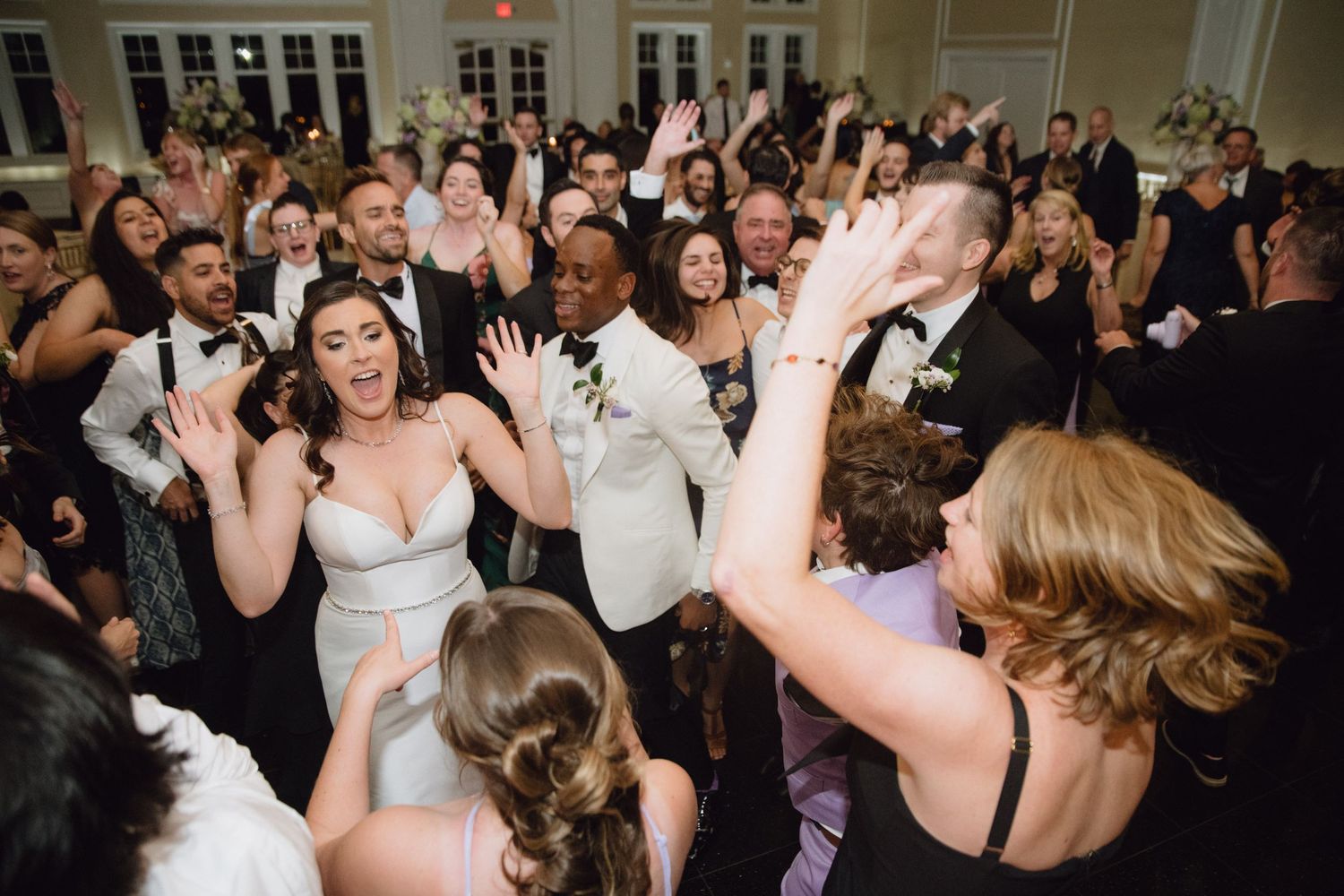 Joyful wedding reception dance floor with bride in white gown surrounded by elegantly dressed guests celebrating.