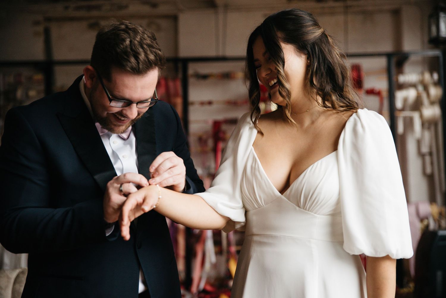 Groom placing wedding ring on brides finger during intimate ceremony, both dressed in elegant wedding attire.