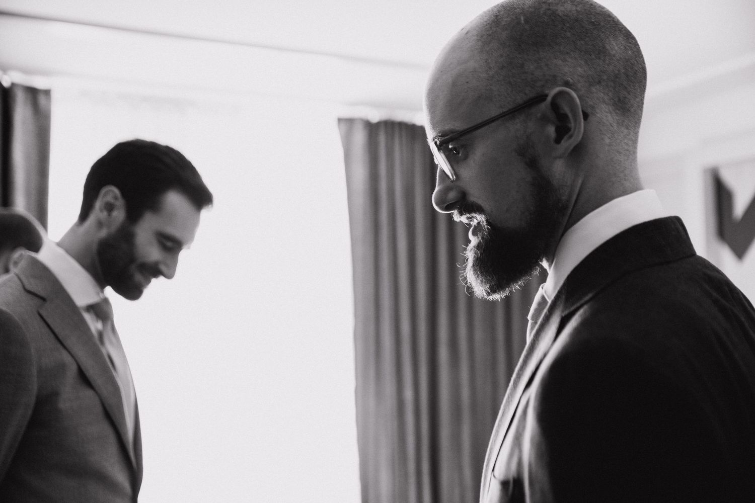 Two men in suits share a quiet moment in black and white wedding photography.