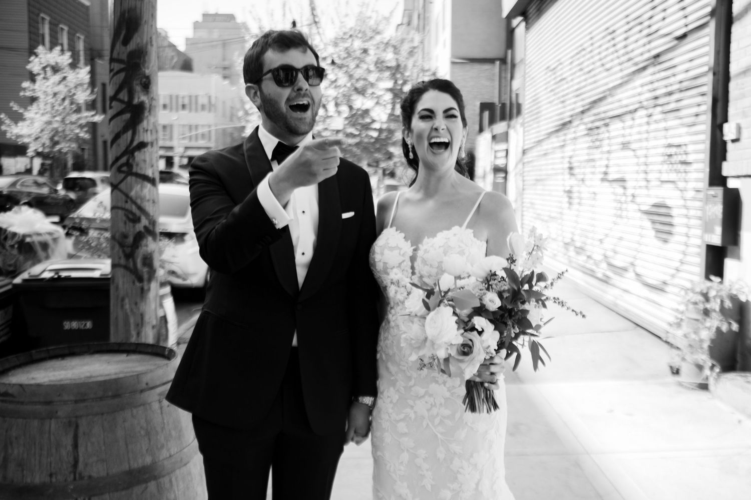 Black and white photo of a joyful bride and groom laughing together on a city sidewalk on their wedding day.
