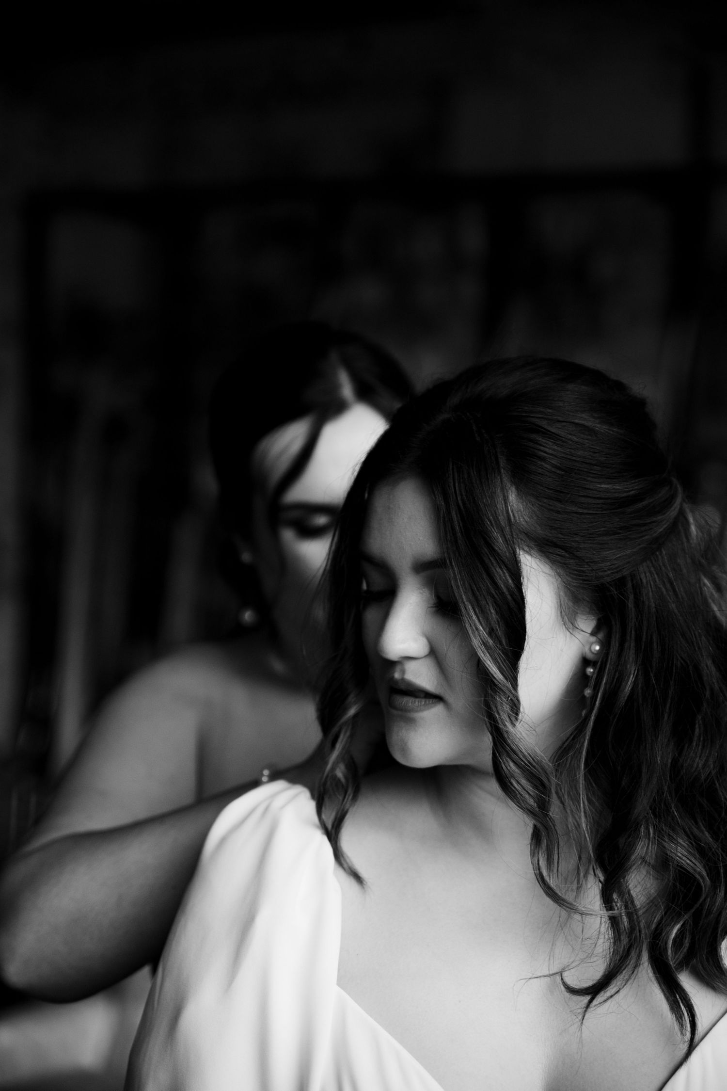 Black and white photo of a bride in a white dress being helped by a bridesmaid during wedding preparations.