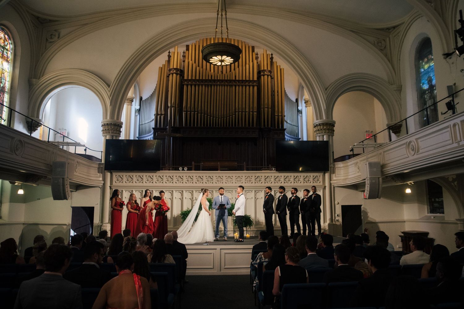 Wedding ceremony in a grand church with pipe organ, bride and groom at altar flanked by bridesmaids and groomsmen.