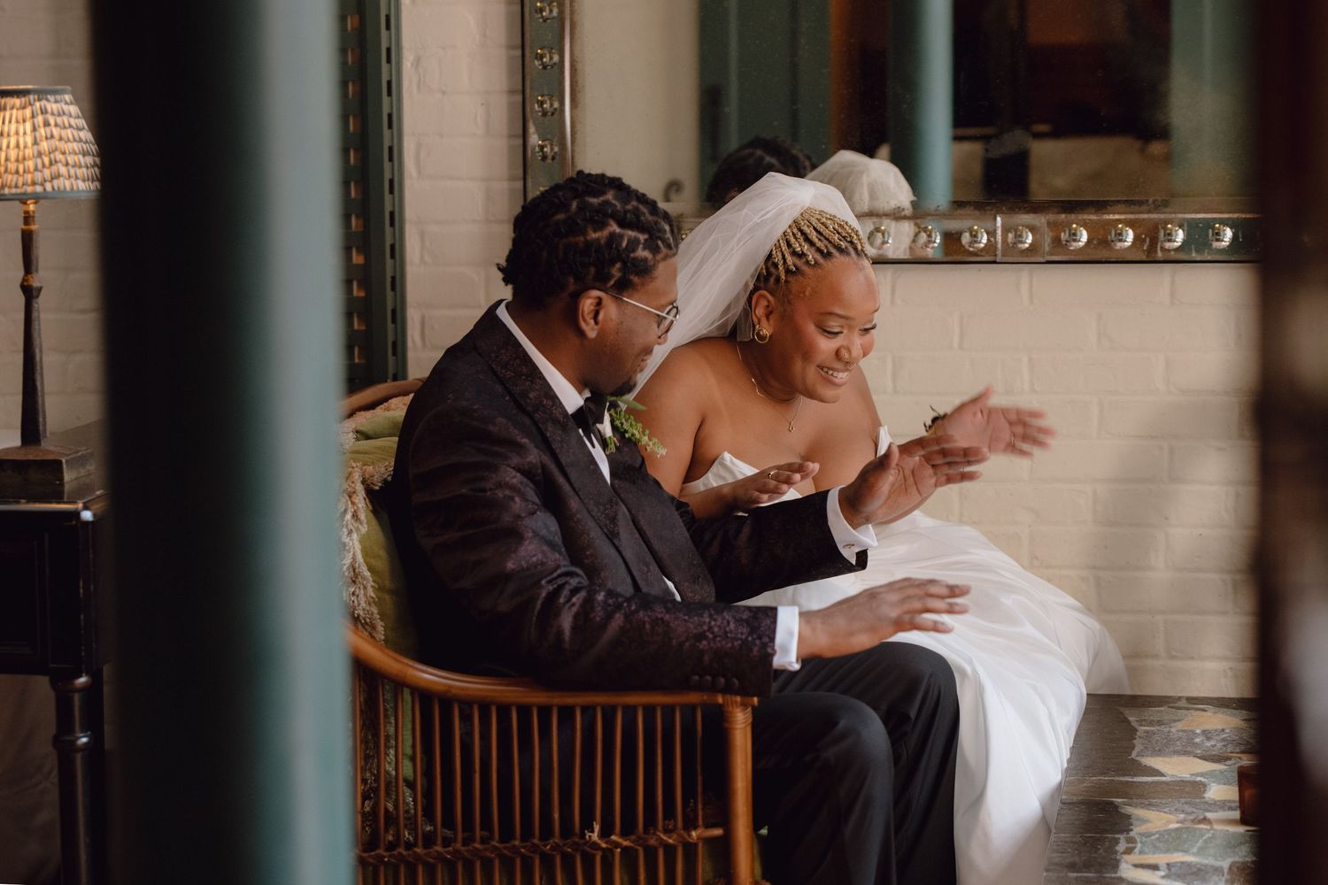 Bride and groom share an intimate moment seated together, with the bride in a white gown and veil leaning toward the groom.