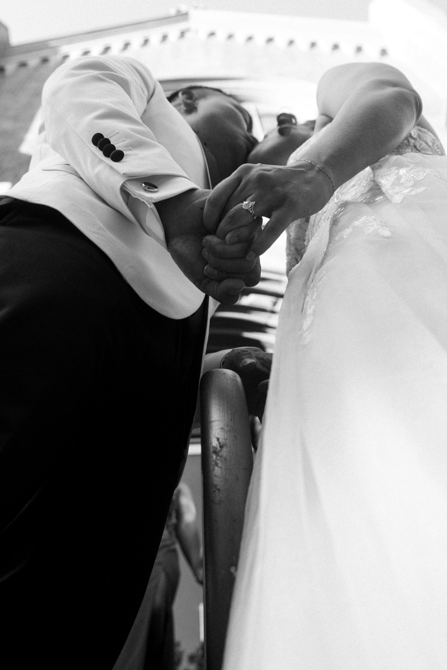 Black and white photo of groom kissing bride's hand on wedding day staircase.
