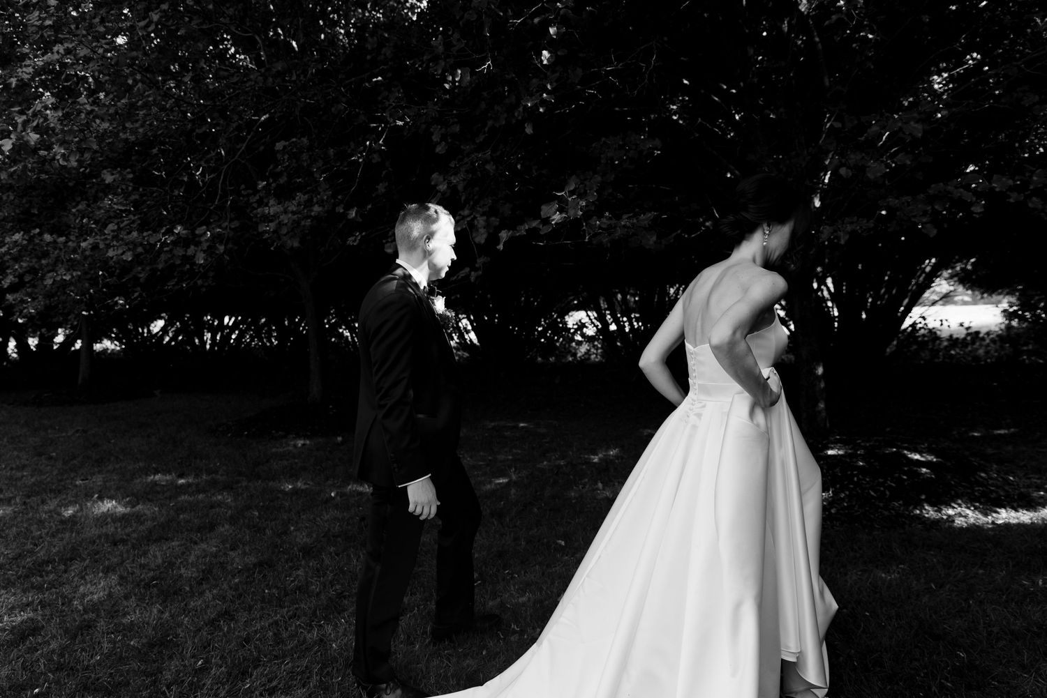 Black and white photo of a bride and groom sharing a first look moment under trees on their wedding day.